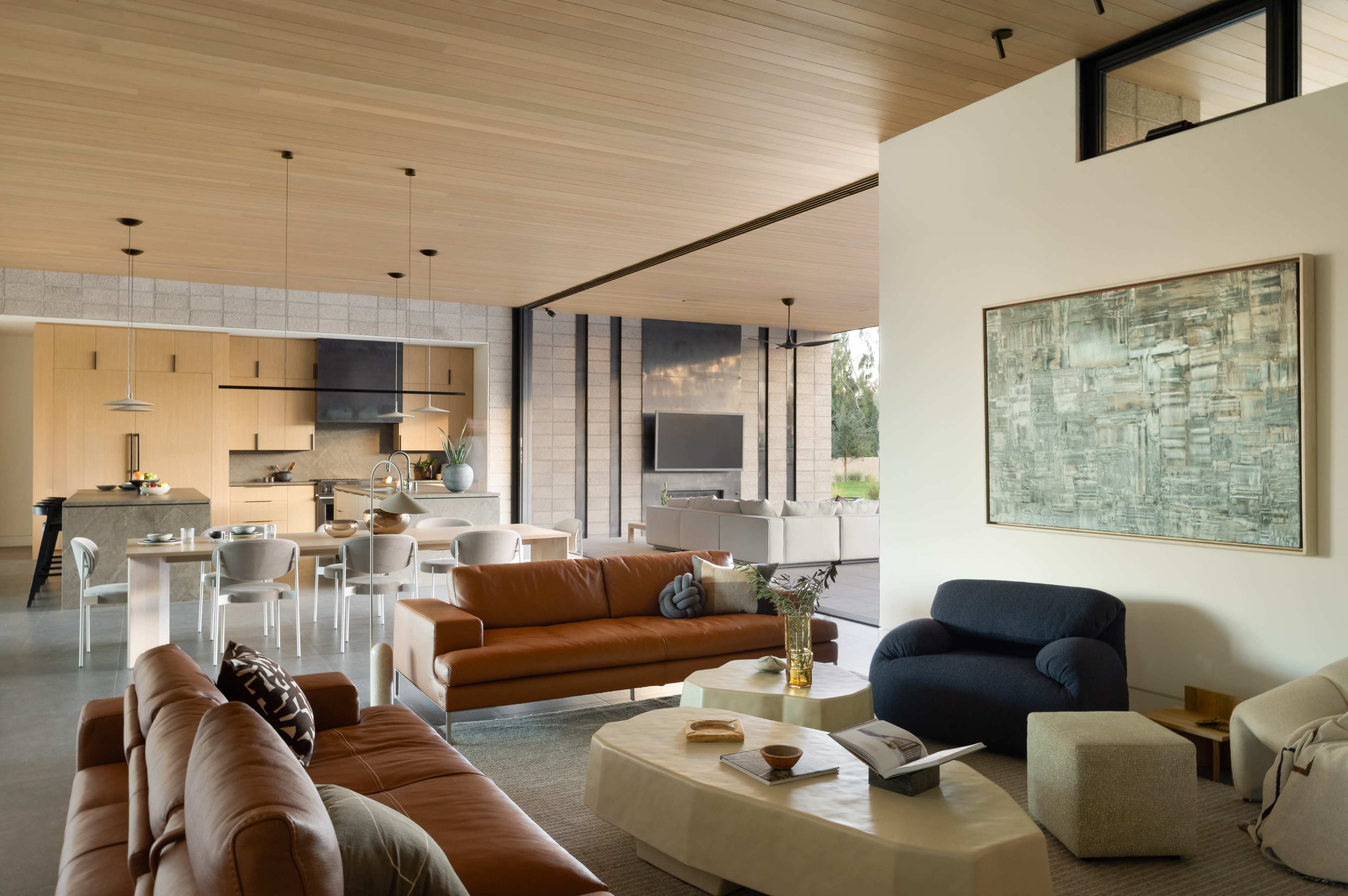 The image depicts a modern living space with a spacious open floor plan, featuring leather sofas, a minimalist coffee table, and an adjoining kitchen area with contemporary furnishings.