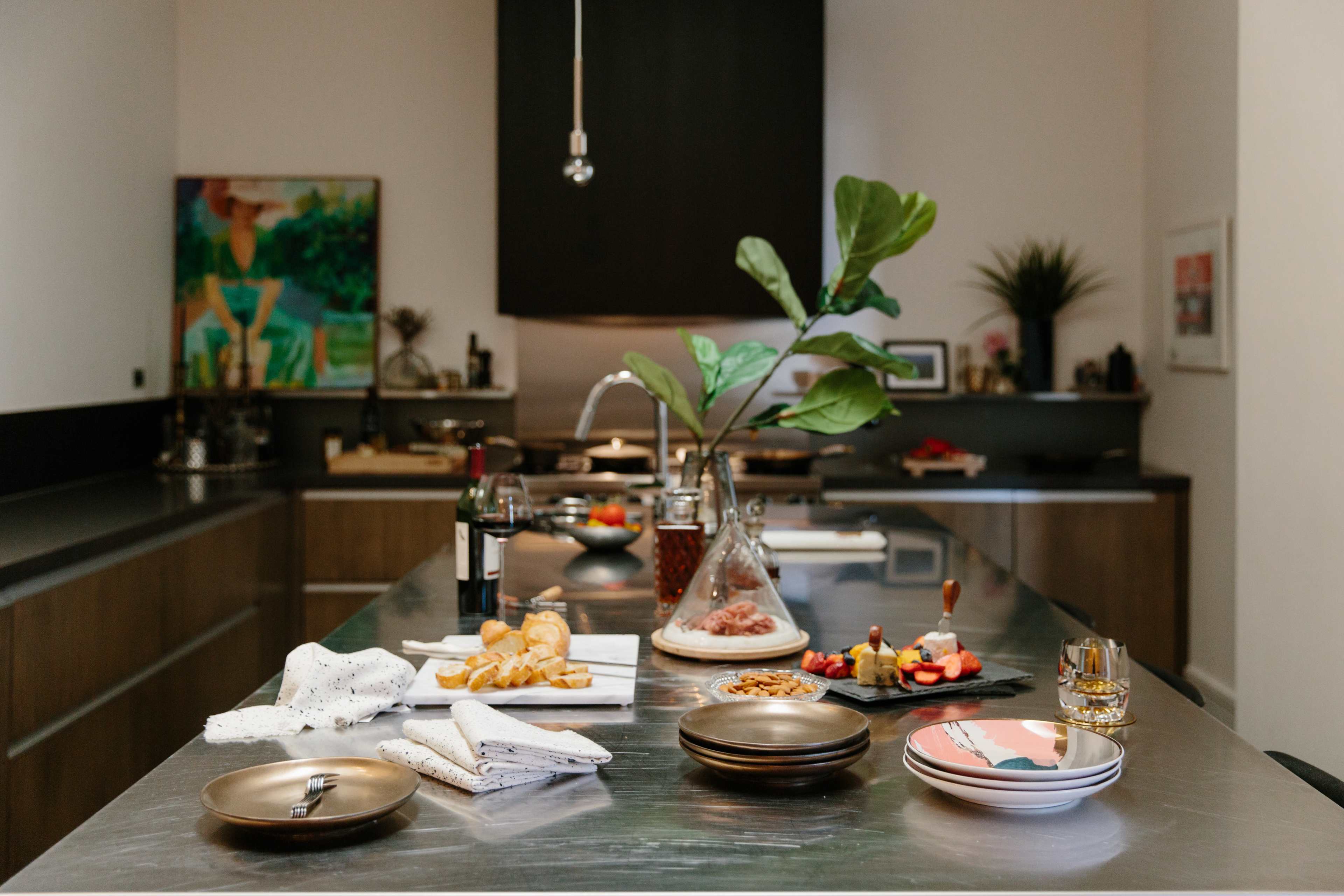 A modern kitchen with a central island featuring a variety of food items, a bottle of wine, and a vase with a green plant.
