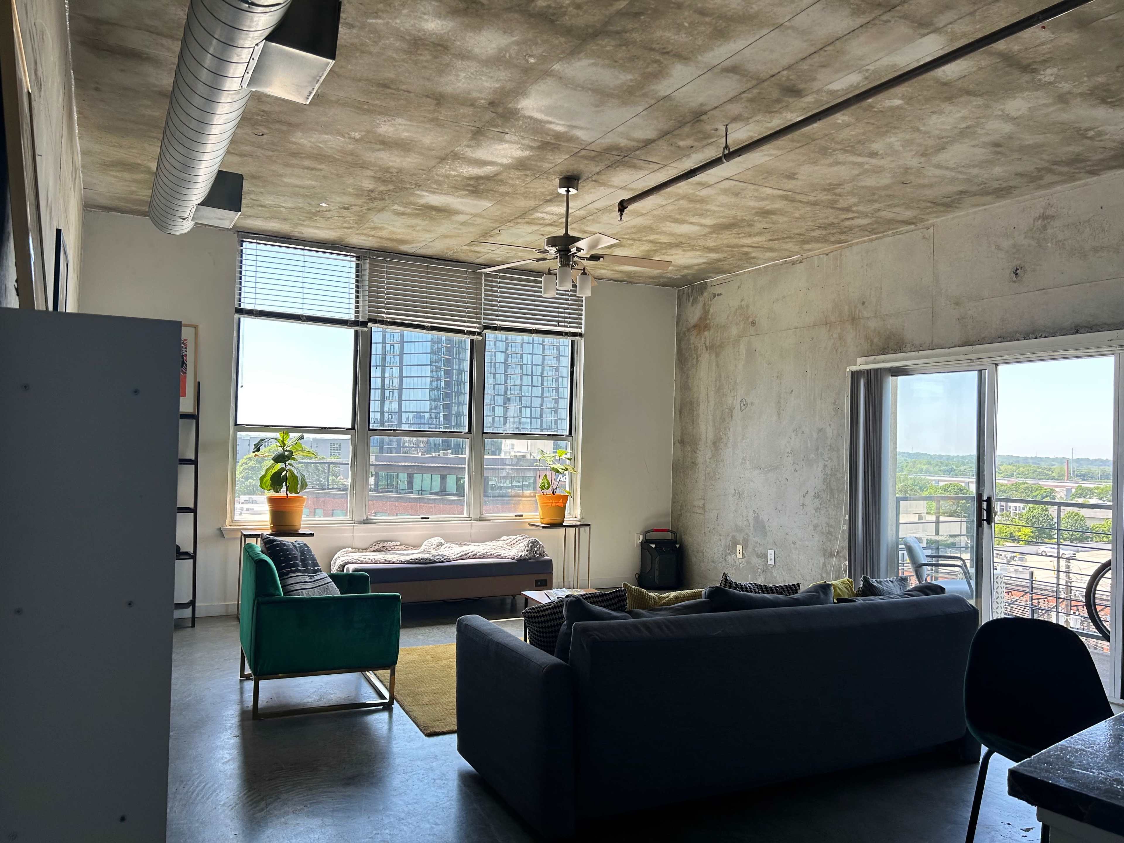The spacious living area features a green couch, a gray couch, and large windows with a view of the city skyline.