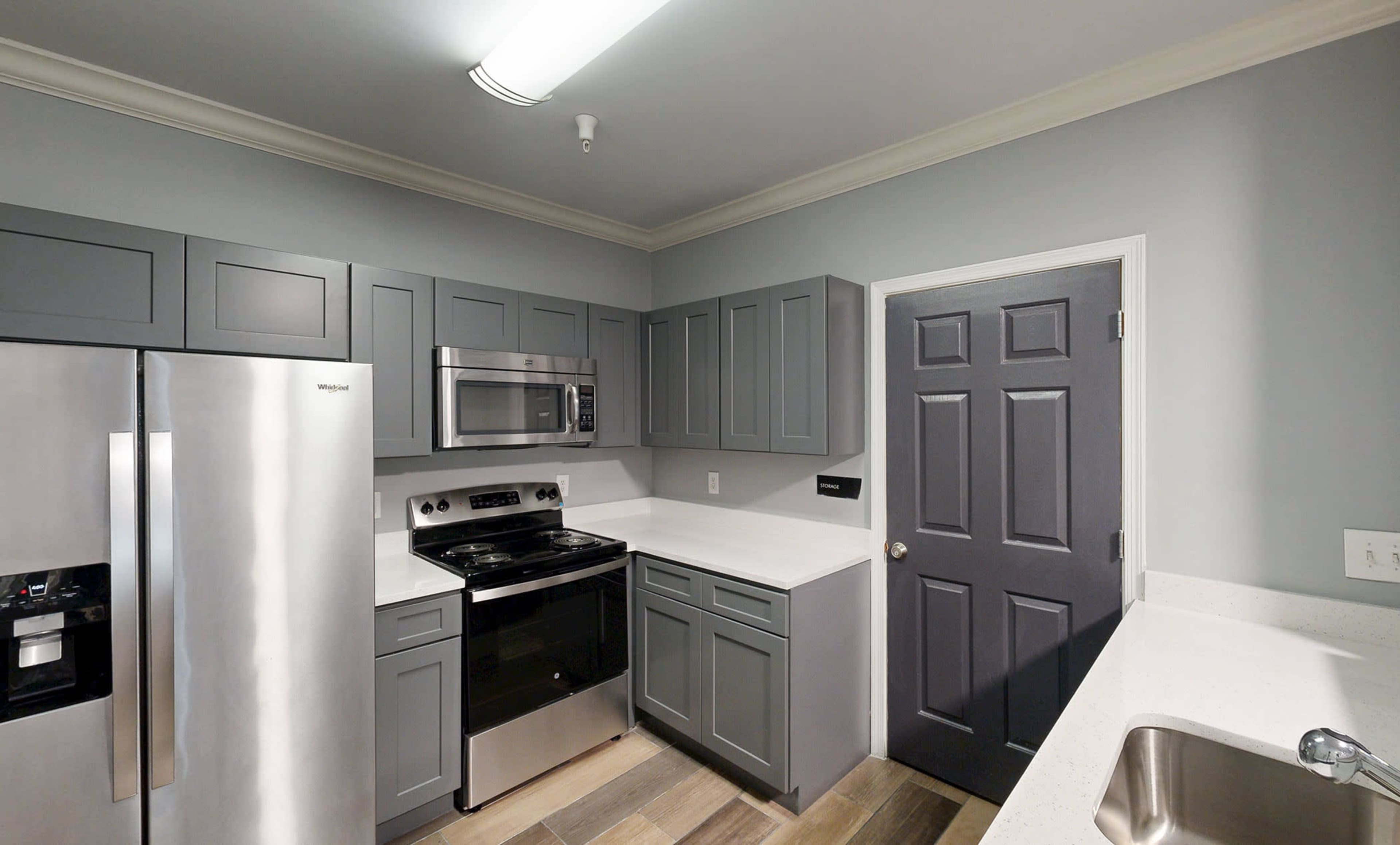The image depicts a modern kitchen featuring gray cabinetry, stainless steel appliances, and a light-colored countertop.