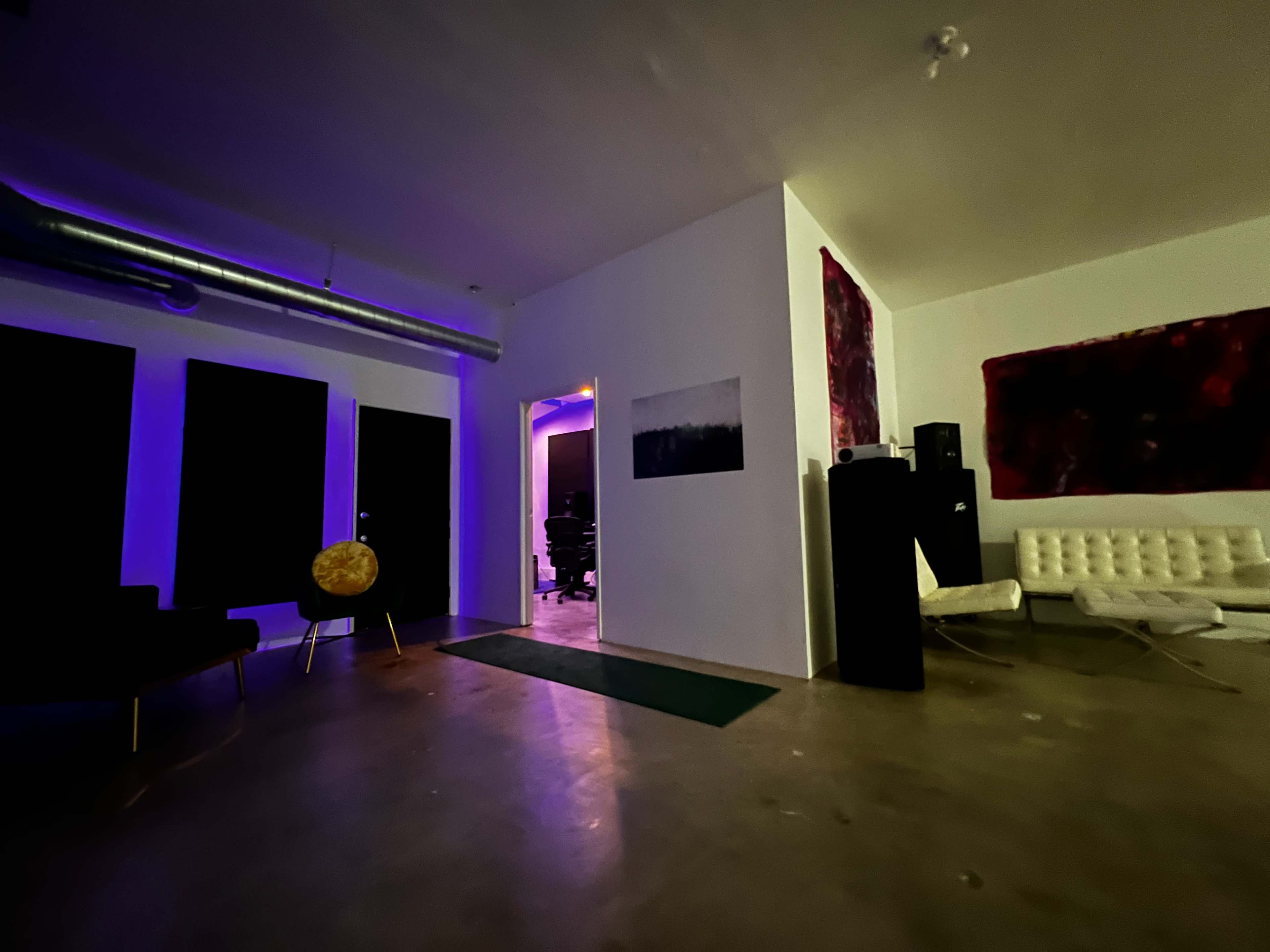 A spacious room with a concrete floor, featuring black wall panels, a white sofa, and a doorway leading to a dimly lit area.