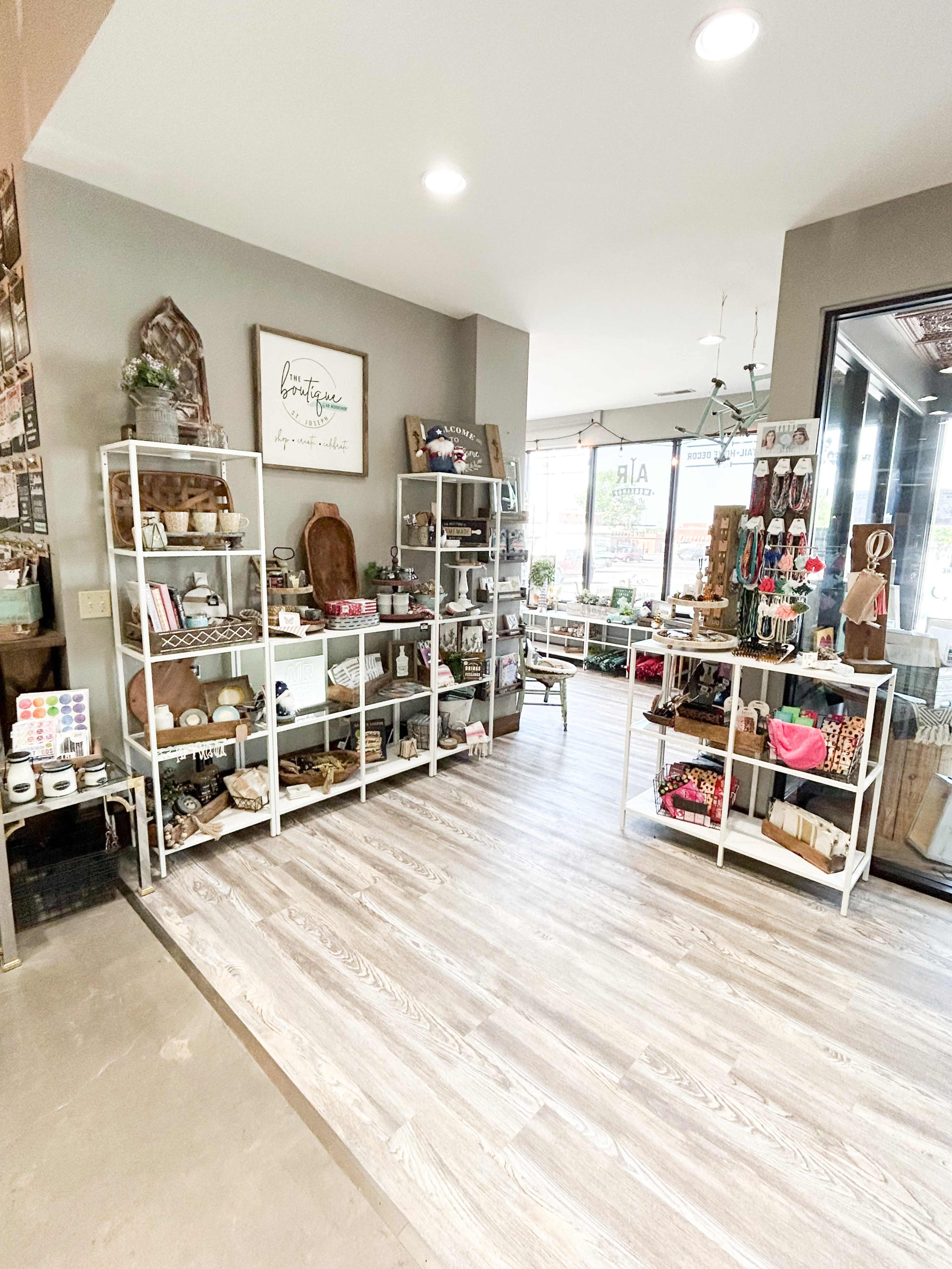 A well-organized retail space featuring shelves filled with various decor items and crafts, with large windows allowing natural light to enter.