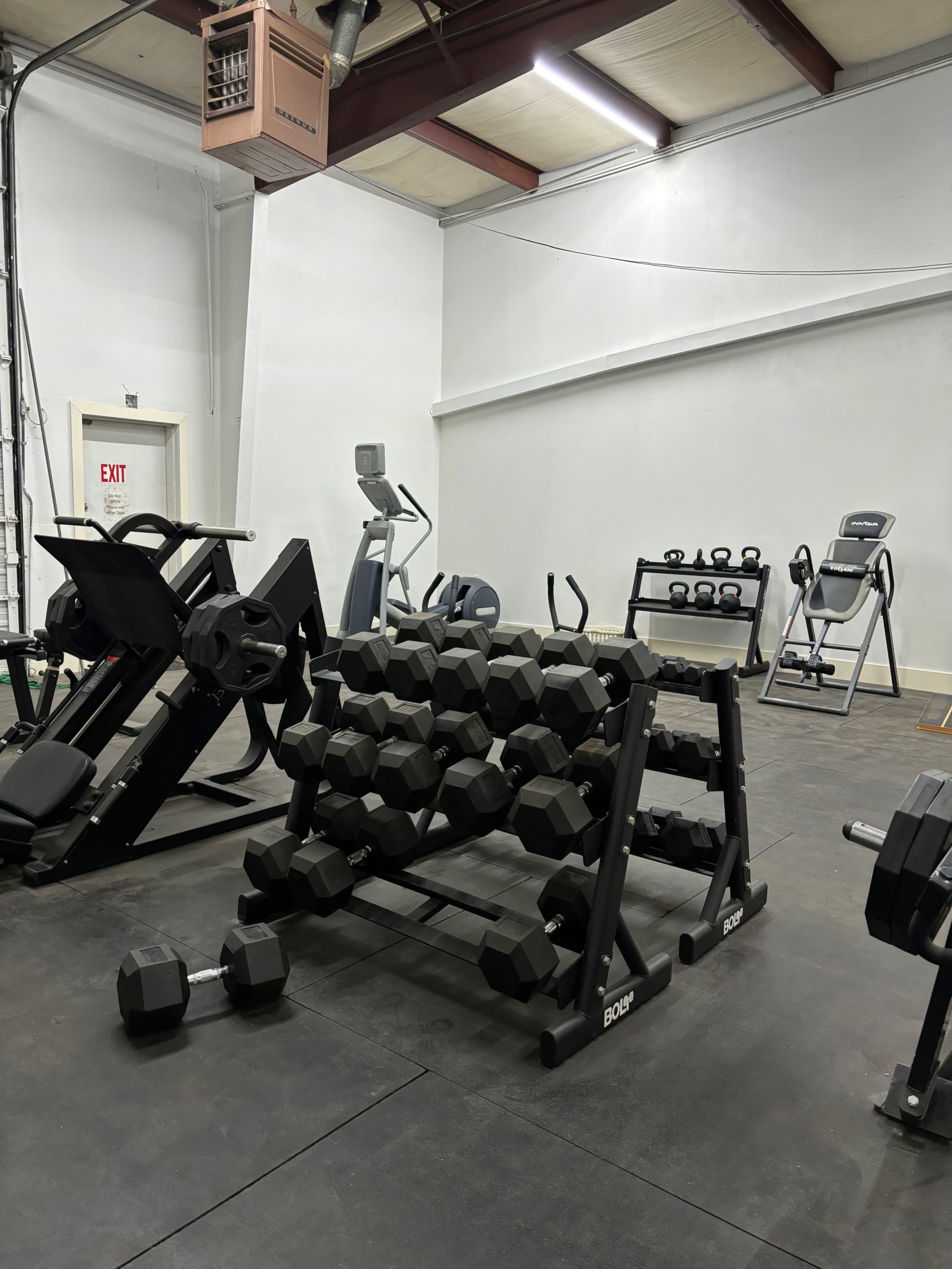 A gym interior with various fitness equipment, including a dumbbell rack, weight machines, and cardio machines.