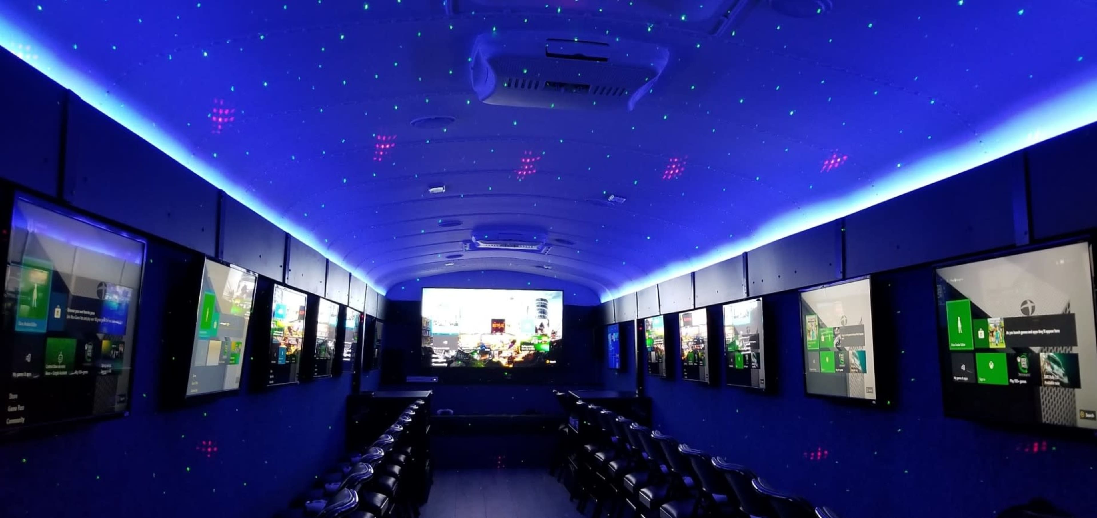 The image shows an interior of a mobile gaming bus featuring multiple screens and LED ambient lighting.