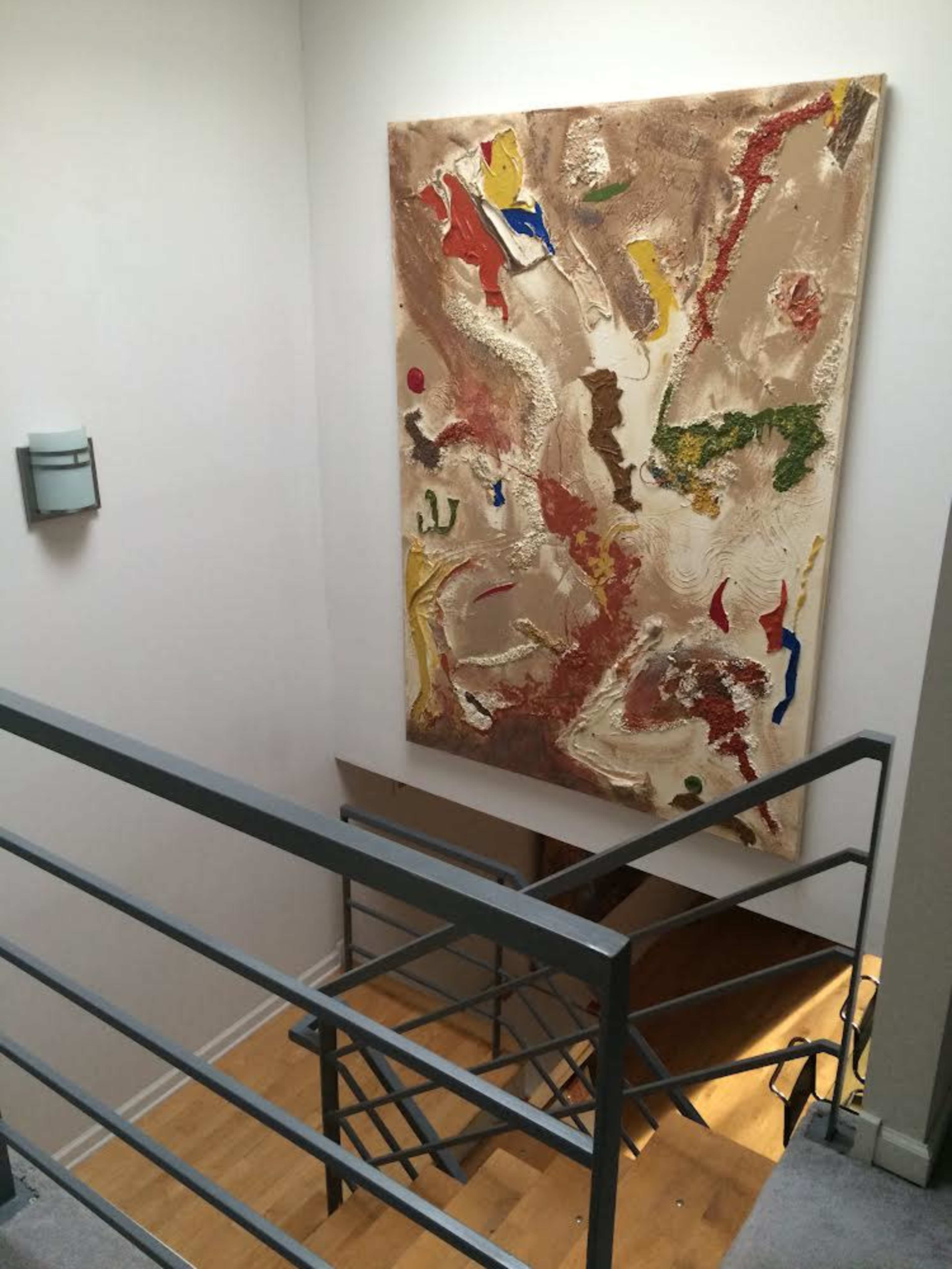 A staircase leading downwards with a large abstract painting on the wall and a metal railing visible in the foreground.