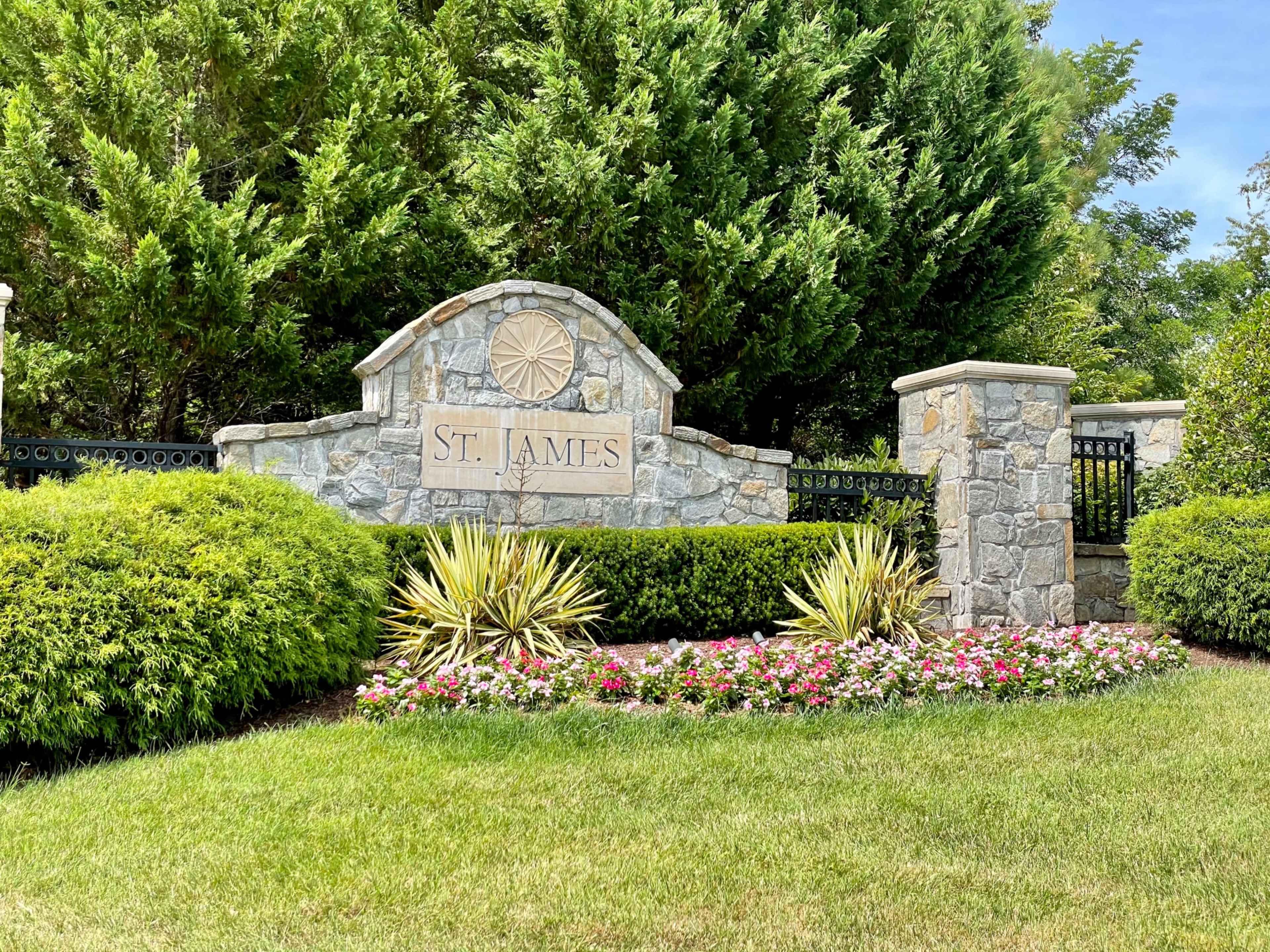 A stone entrance sign reading "St. James" surrounded by neatly trimmed bushes and colorful flowers.
