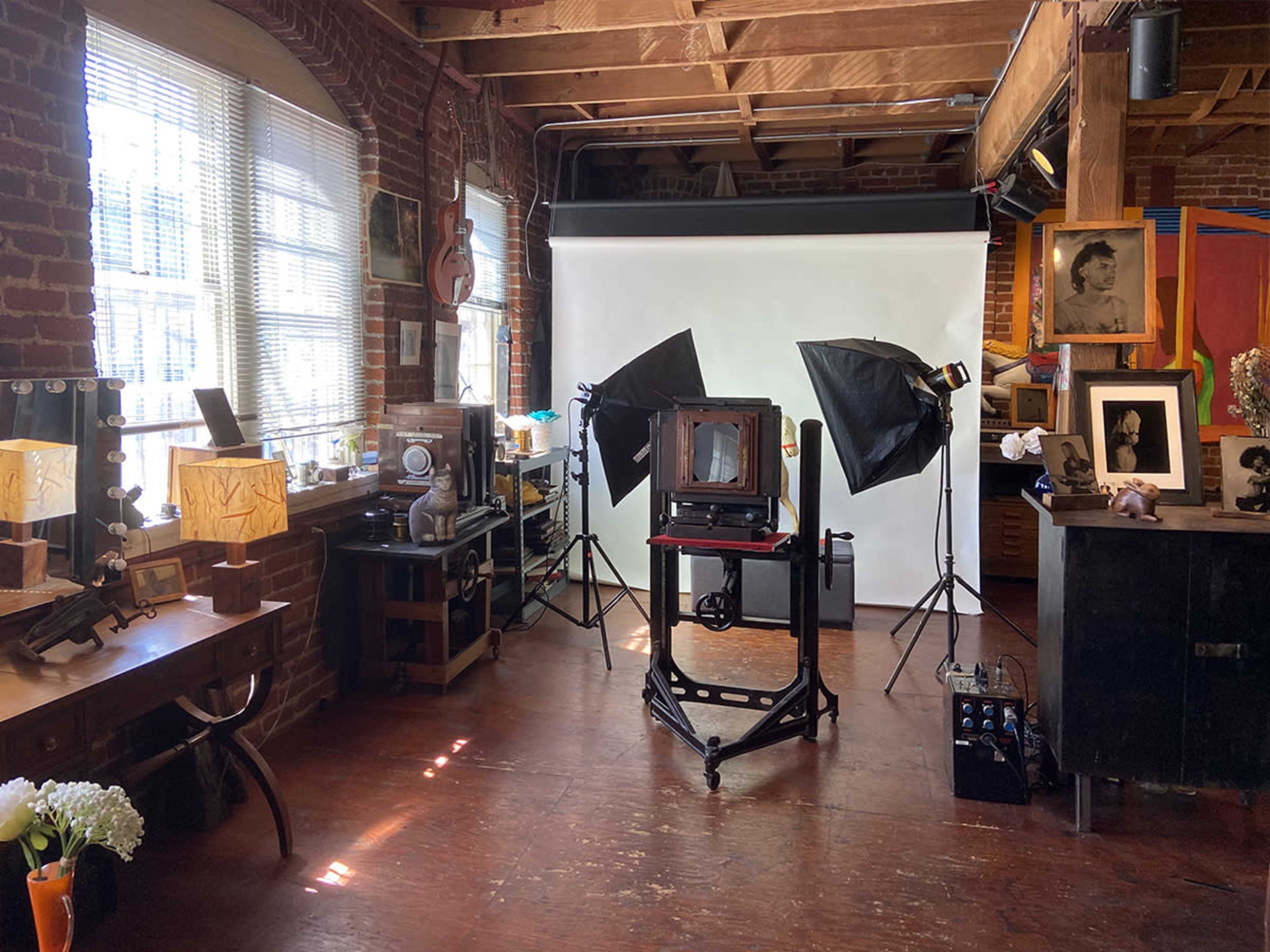 A photography studio with vintage equipment, two light stands, and a white backdrop in a room with exposed brick walls.