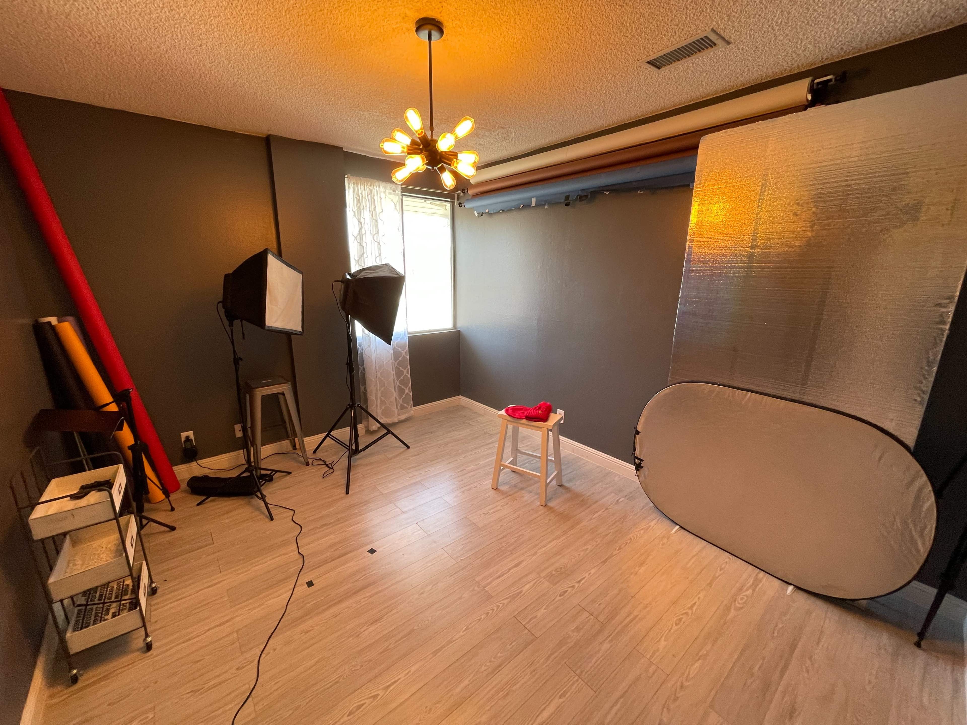 A well-lit photography studio with a backdrop setup, a stool, and two softbox lights.