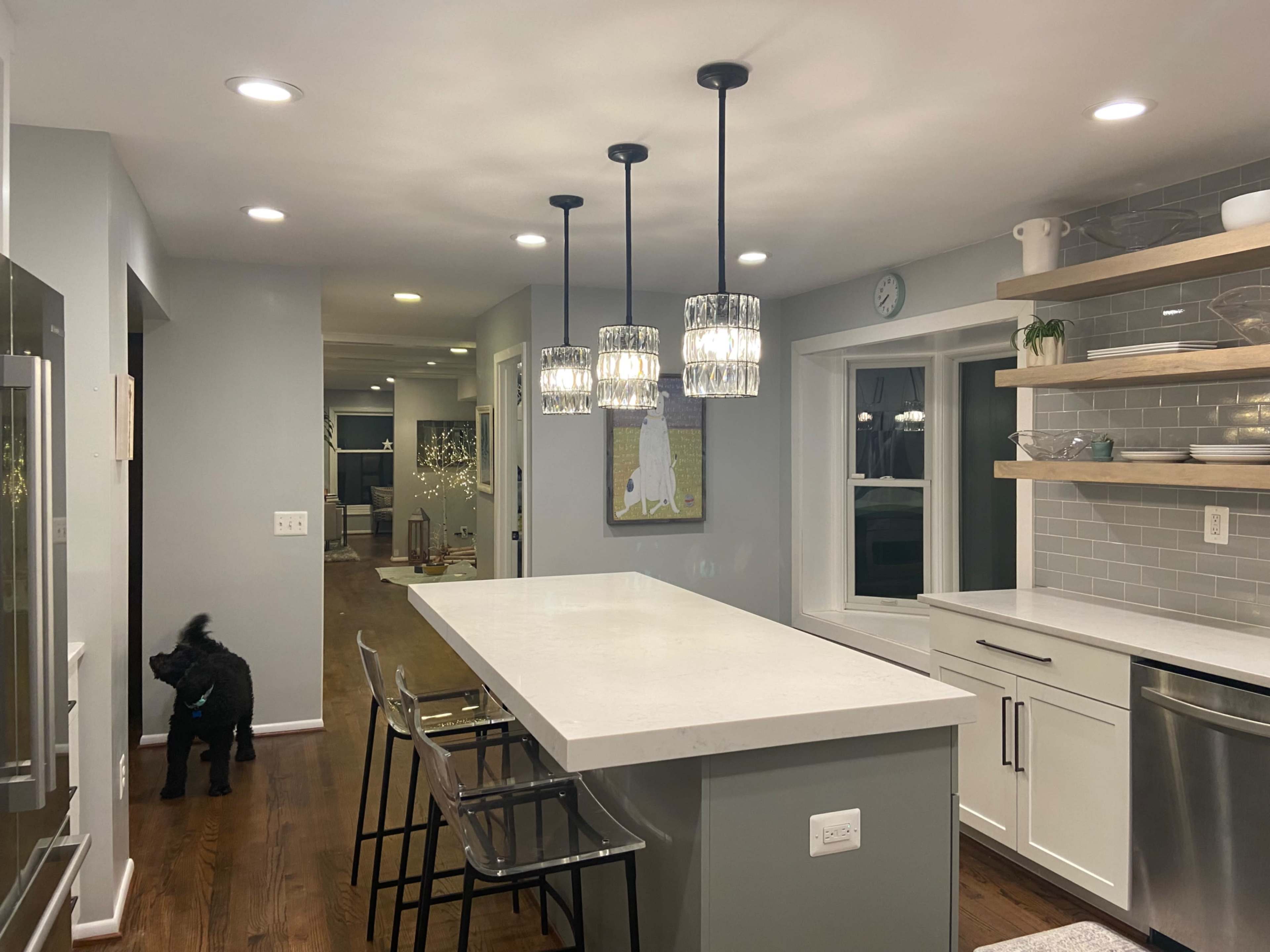 A modern kitchen features an island with three pendant lights, bar stools, and an adjacent dining area with a view of the living space.