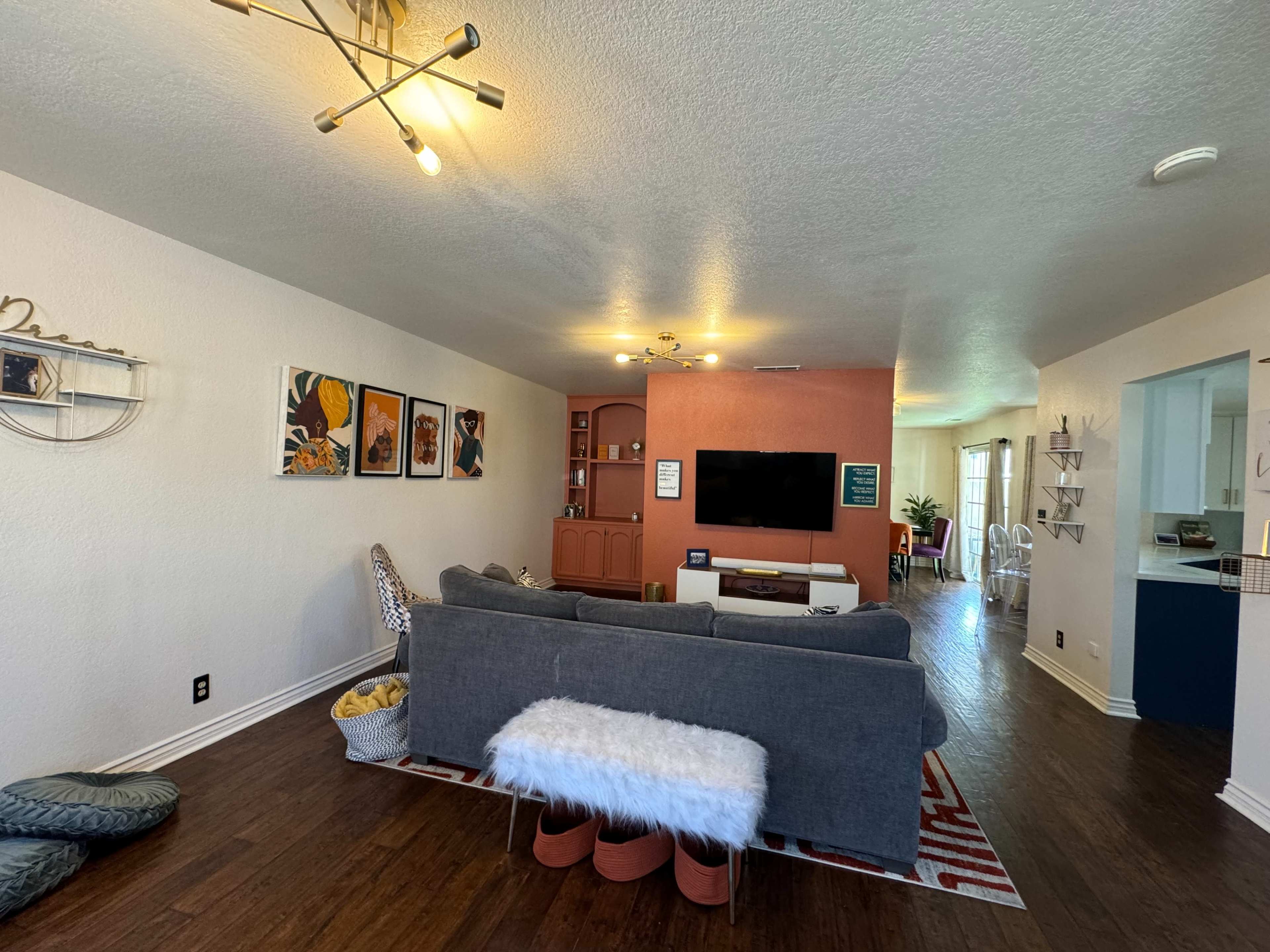 The image shows a living room with a gray sofa, a television mounted on a wall, and a dining area visible in the background.