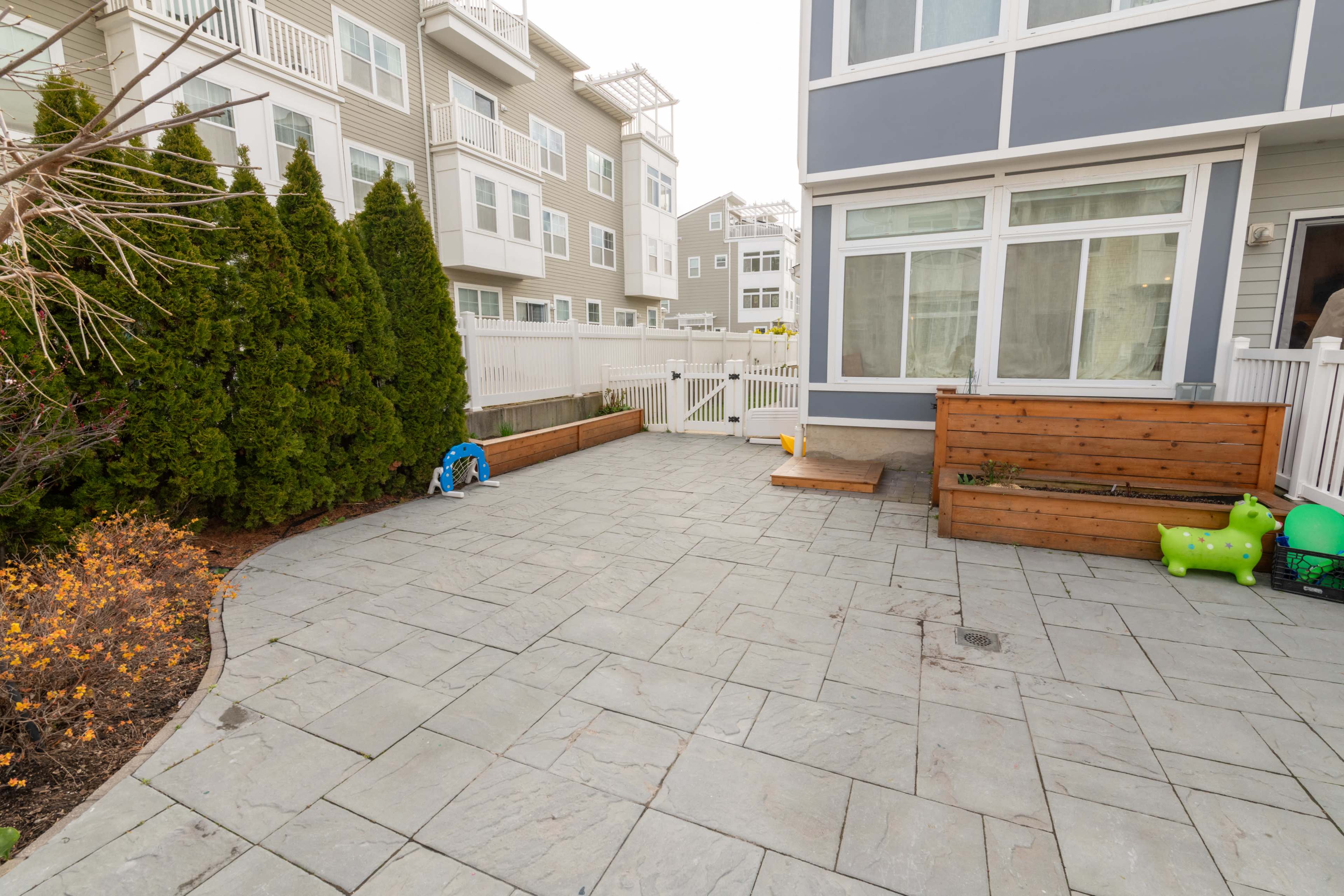 The image shows a paved outdoor patio area with wooden benches and green decorative elements, surrounded by multi-story residential buildings.