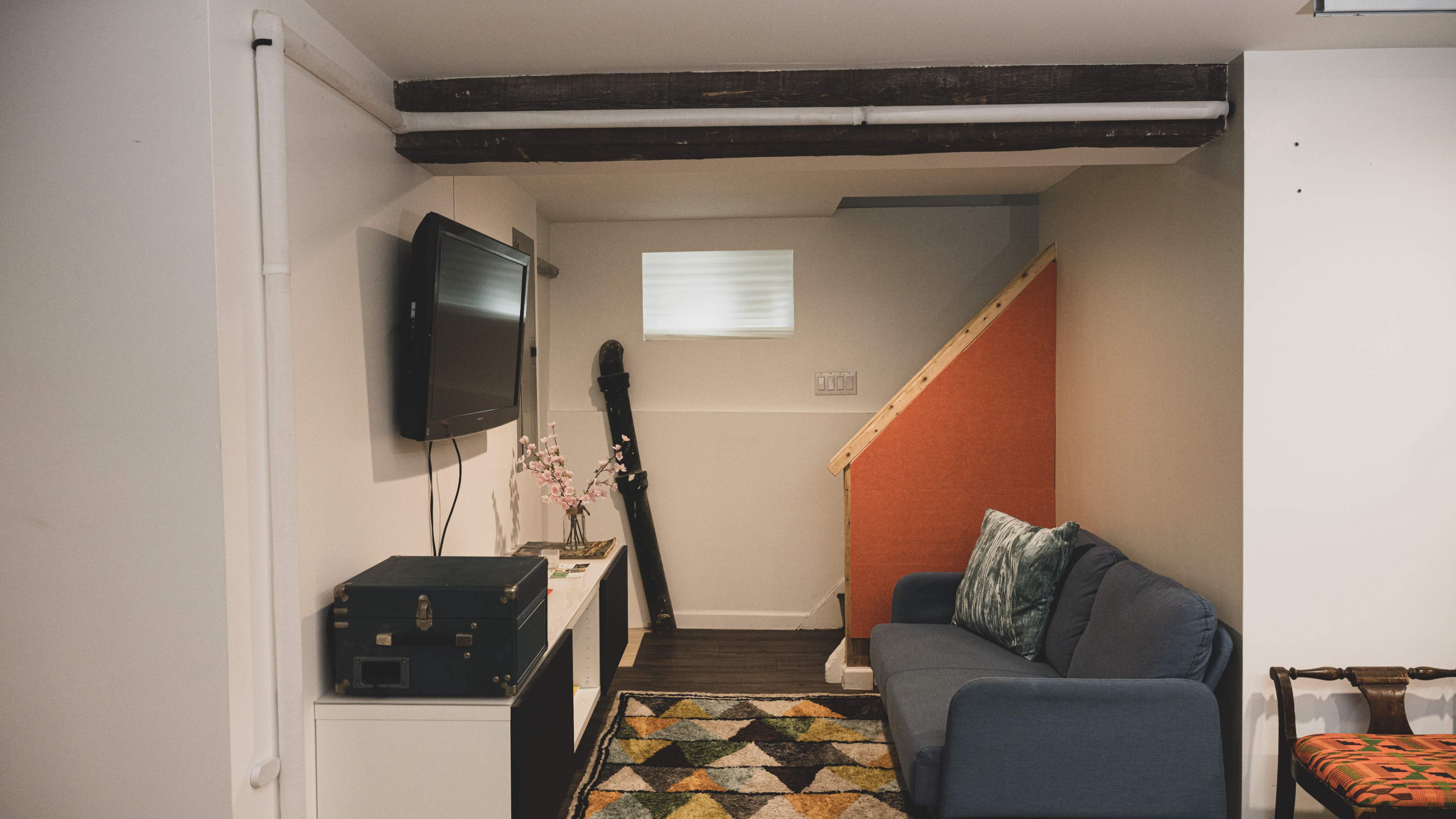 A small basement living area features a blue sofa, a television mounted on the wall, and a staircase leading to another level.