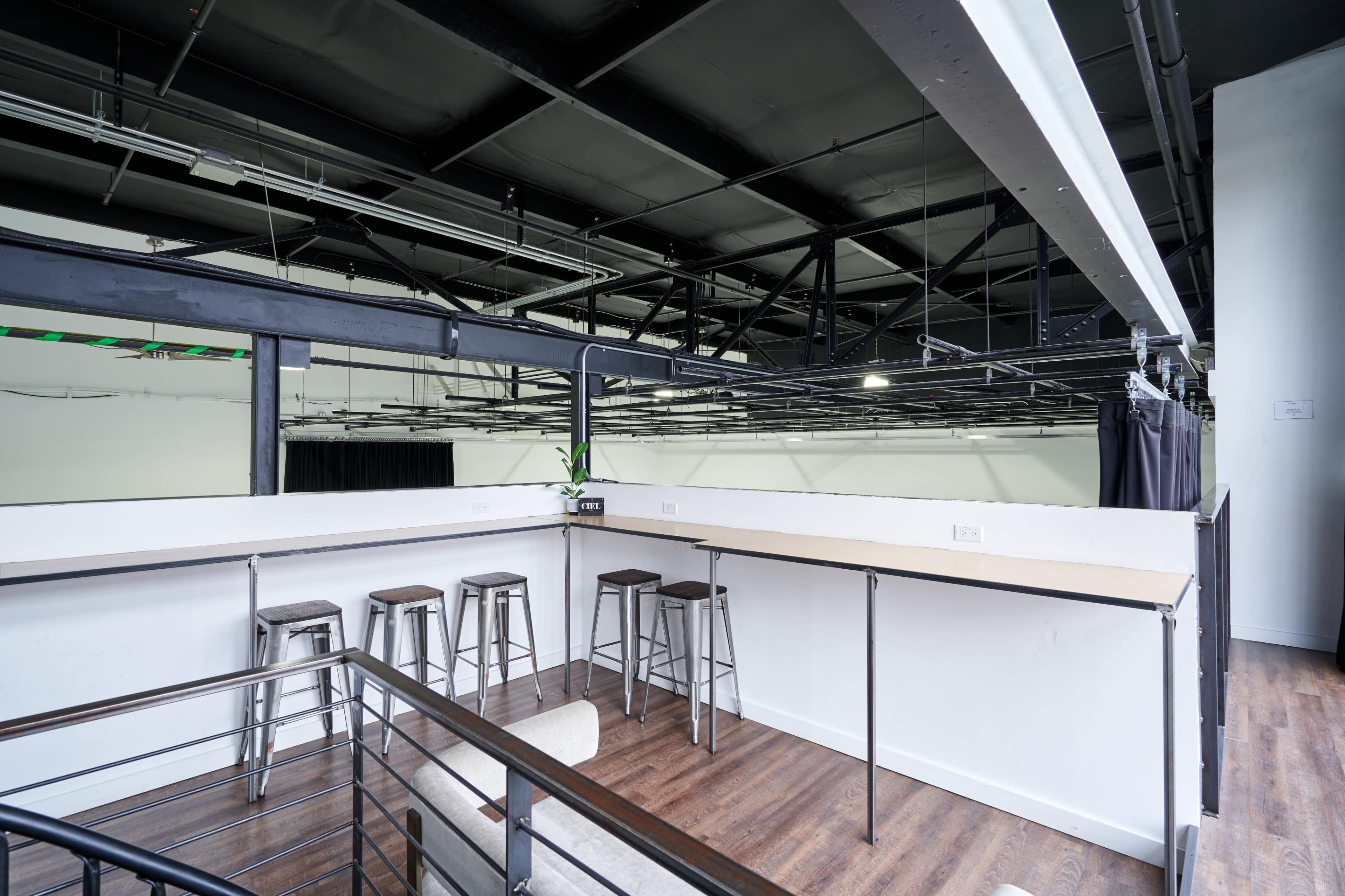 A spacious loft-style area features a bar-height countertop with metal stools, overlooking an empty, well-lit room with high ceilings.