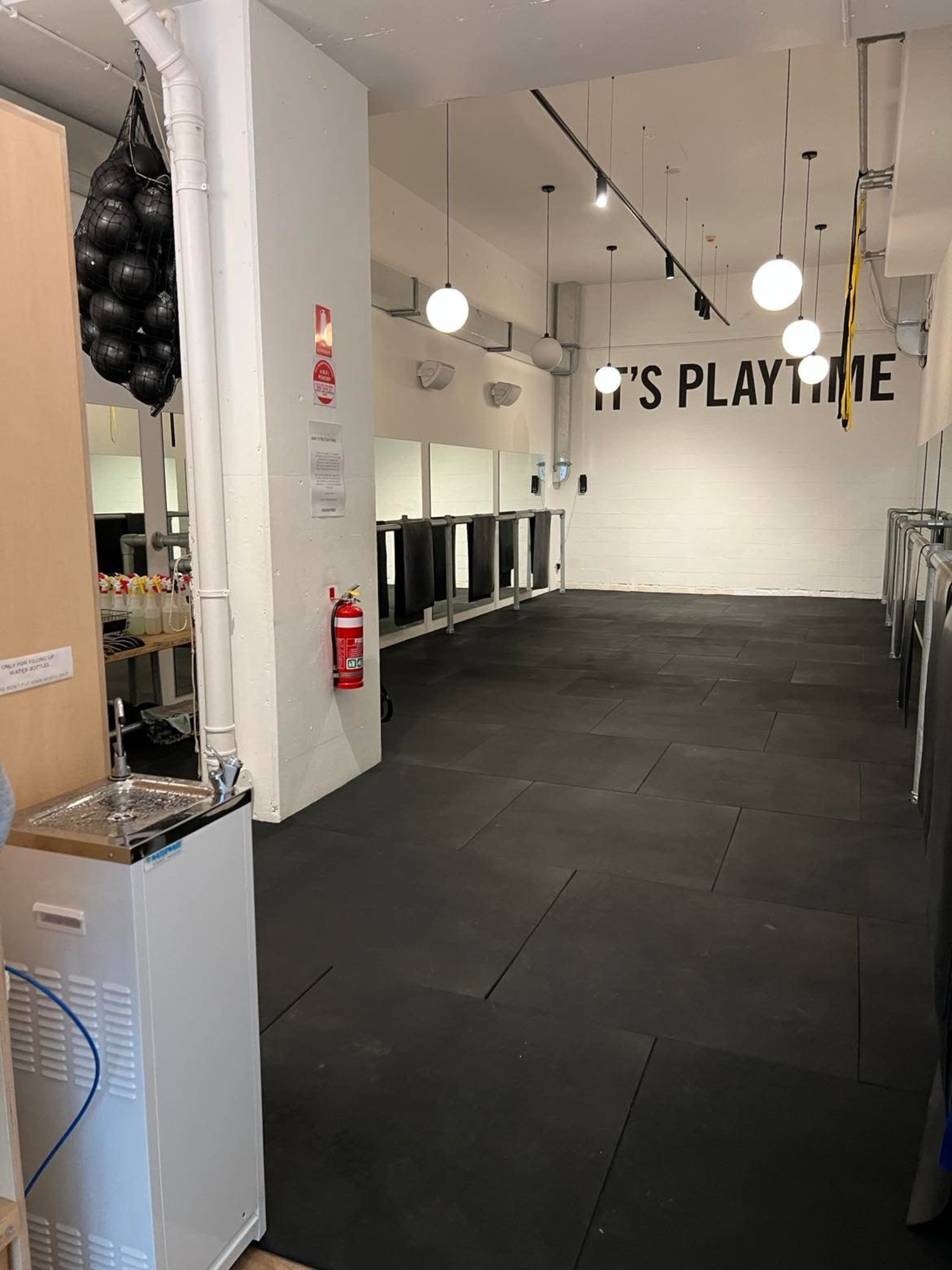 A spacious indoor area with black rubber flooring, ceiling lights, and a wall featuring the text "IT'S PLAYTIME."