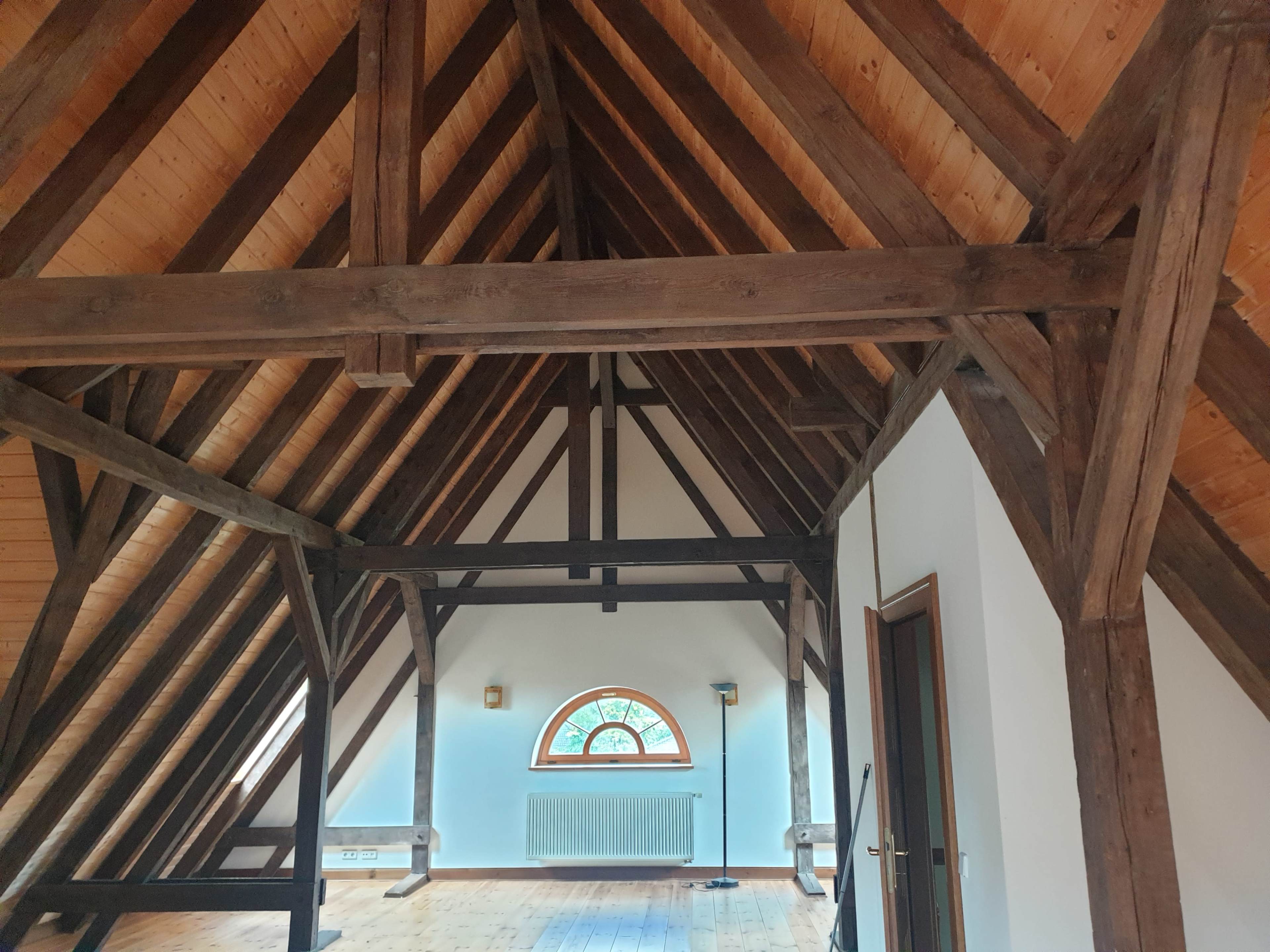 An empty attic with exposed wooden beams and a large arched window.