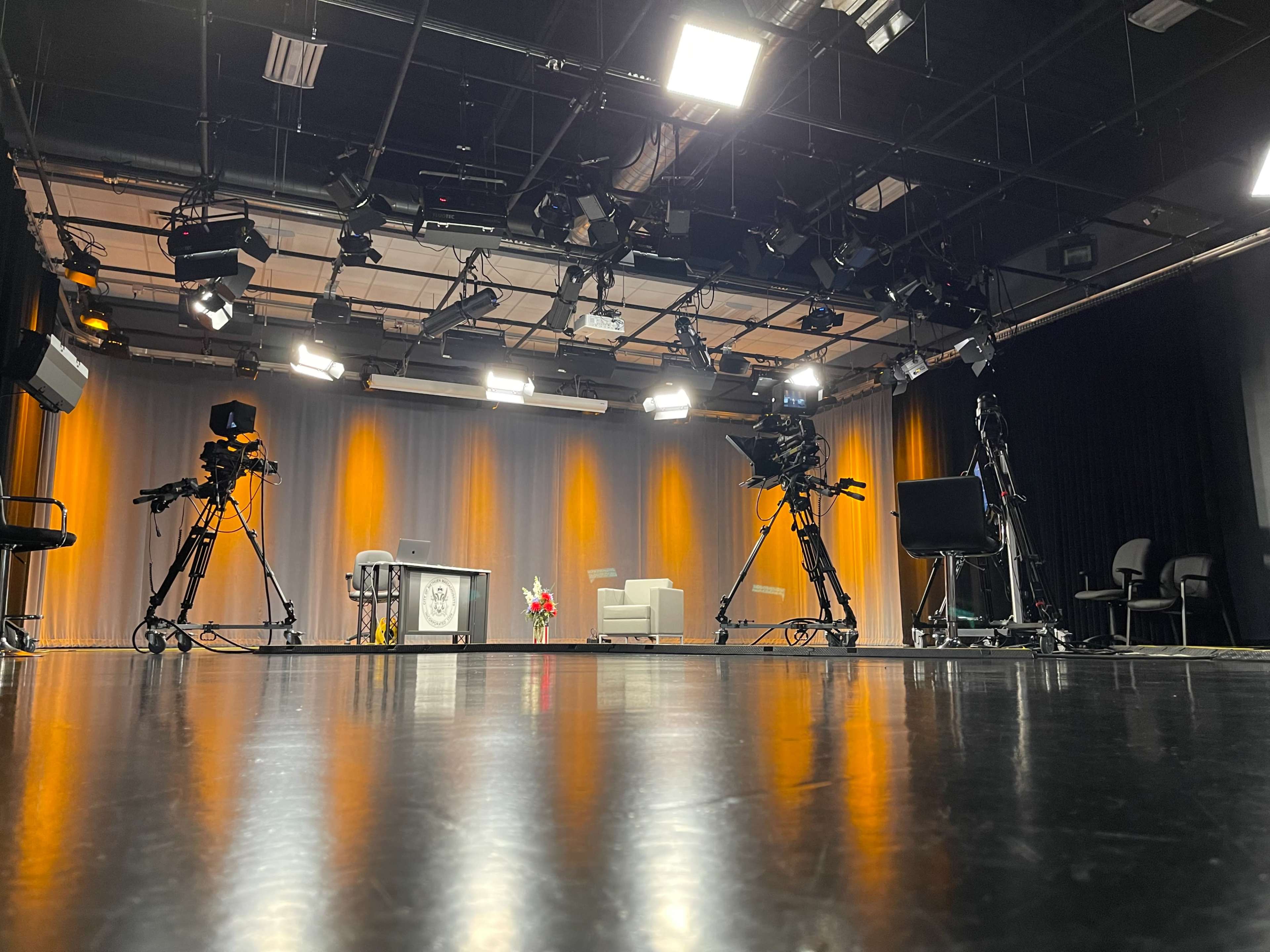 A television studio equipped with cameras, a set featuring a couch and table, and multiple lighting fixtures overhead.