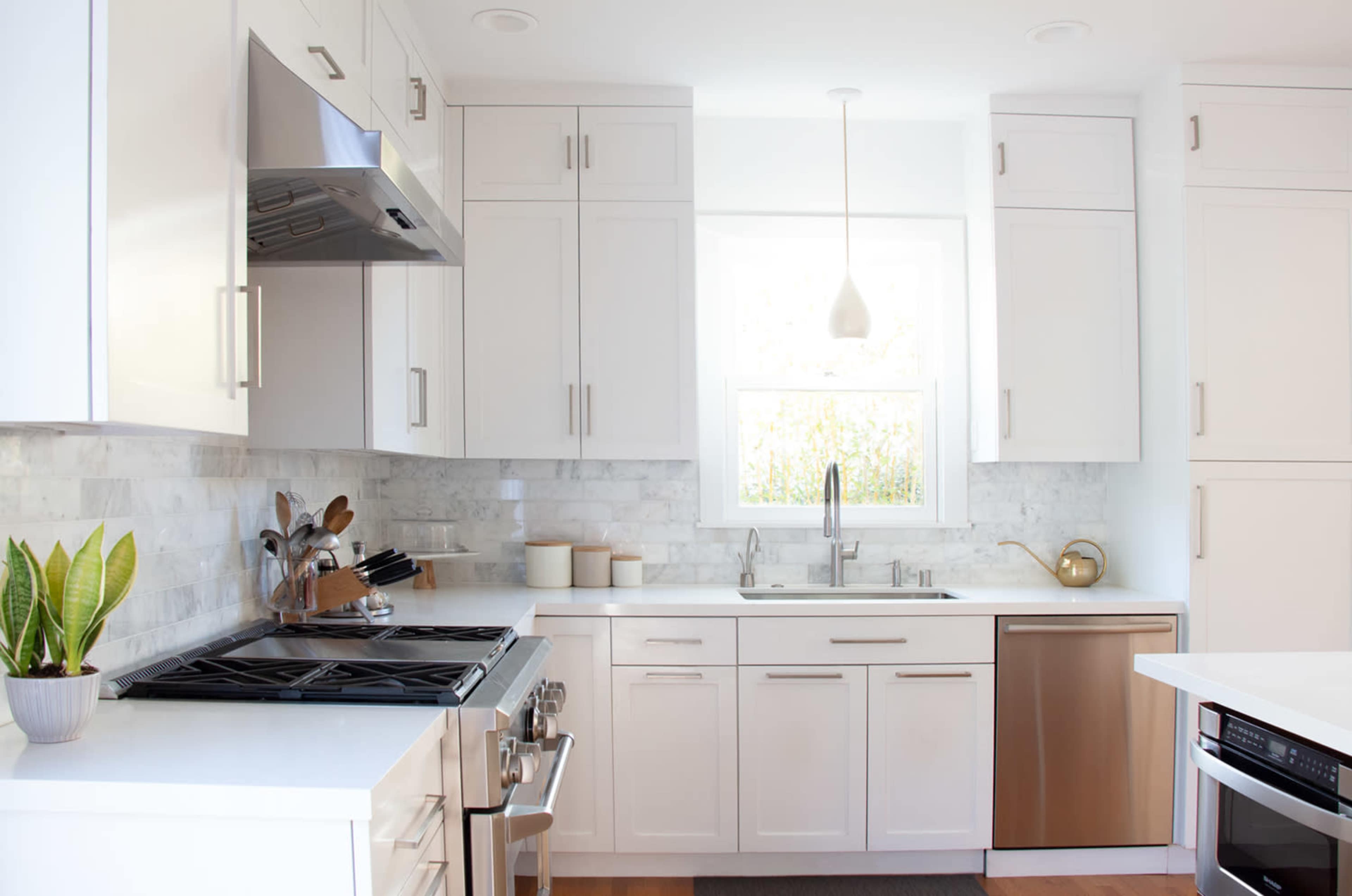 A modern kitchen features white cabinetry, stainless steel appliances, and a window above the sink.