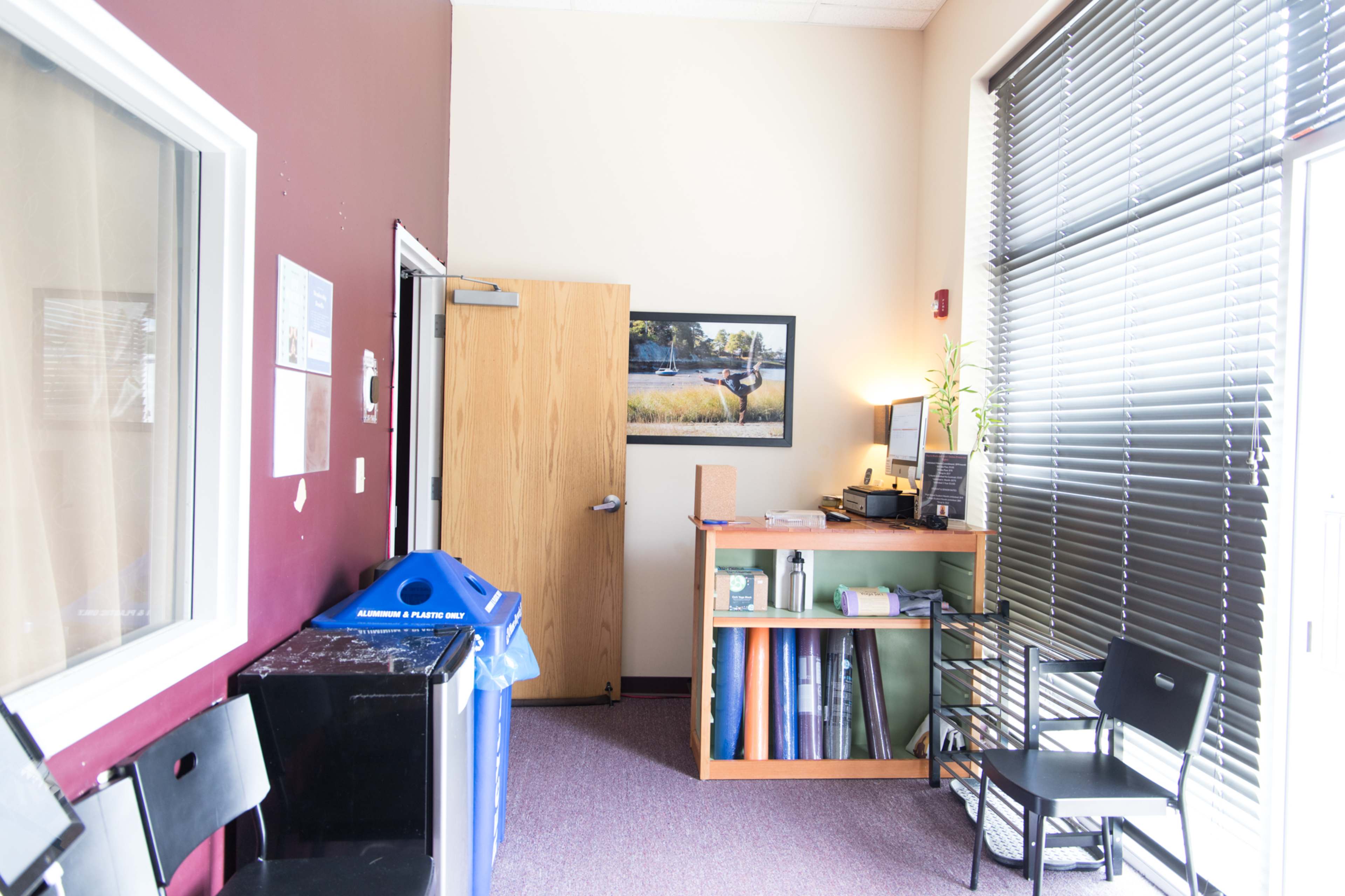 A waiting area with chairs, a desk, a blue recycling bin, and a door leading to another room.