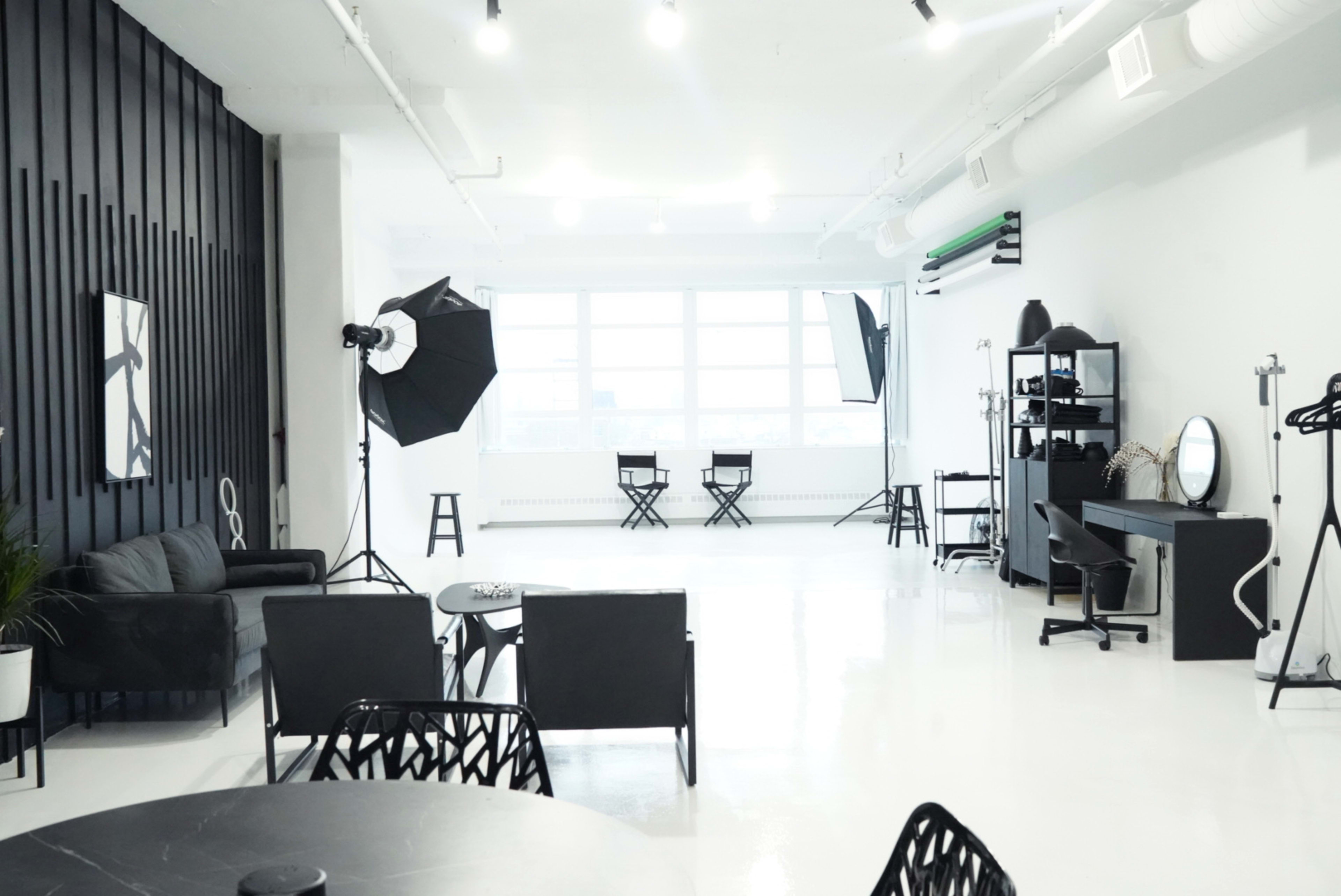 A spacious, modern studio with a bright, white floor, black accent walls, and various photography equipment arranged throughout.