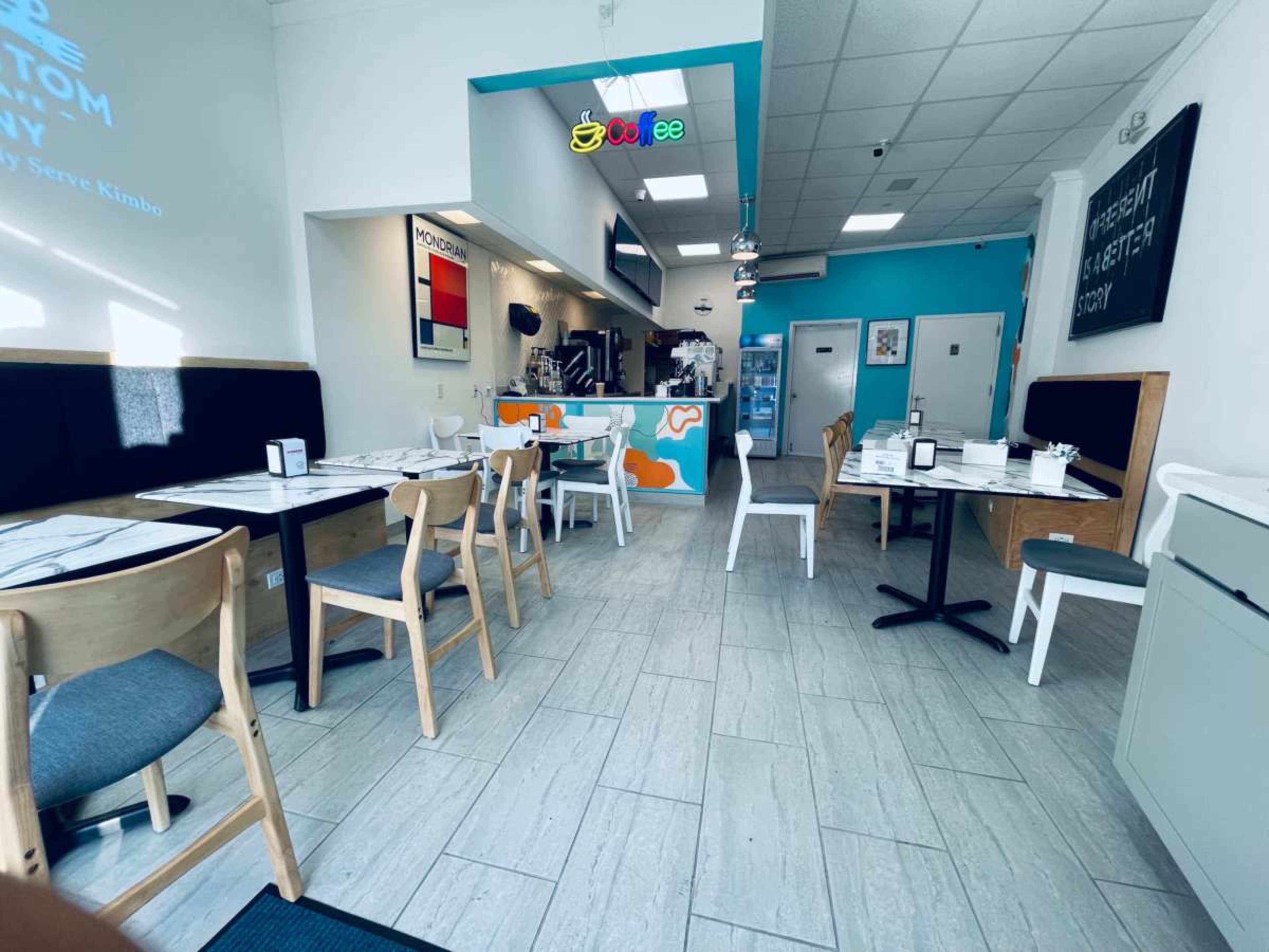 The image shows a modern café interior with a mixture of tables and chairs, featuring a brightly colored counter in the back.