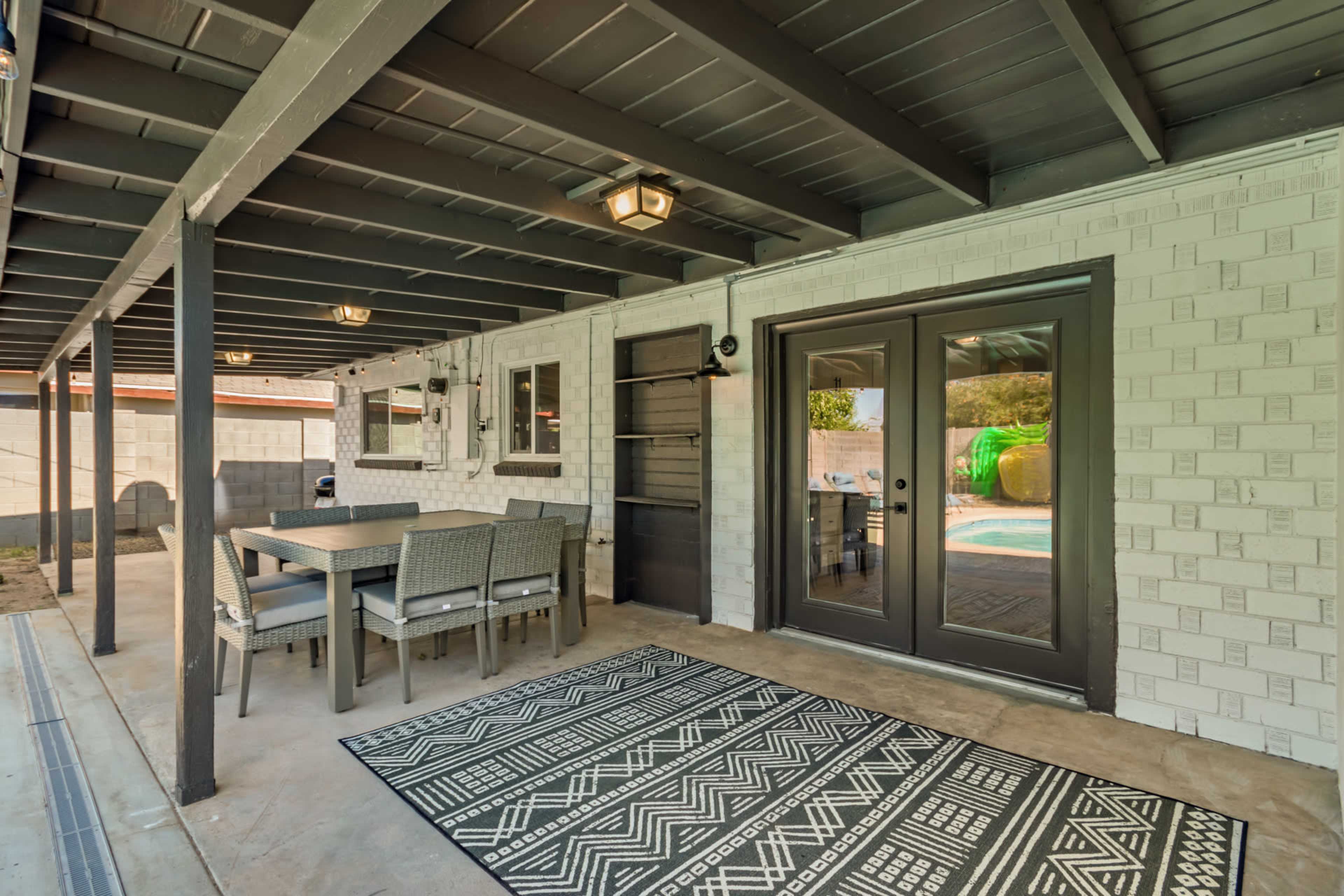 A covered patio area featuring a table and chairs, a patterned rug, and sliding glass doors that open to a pool area.