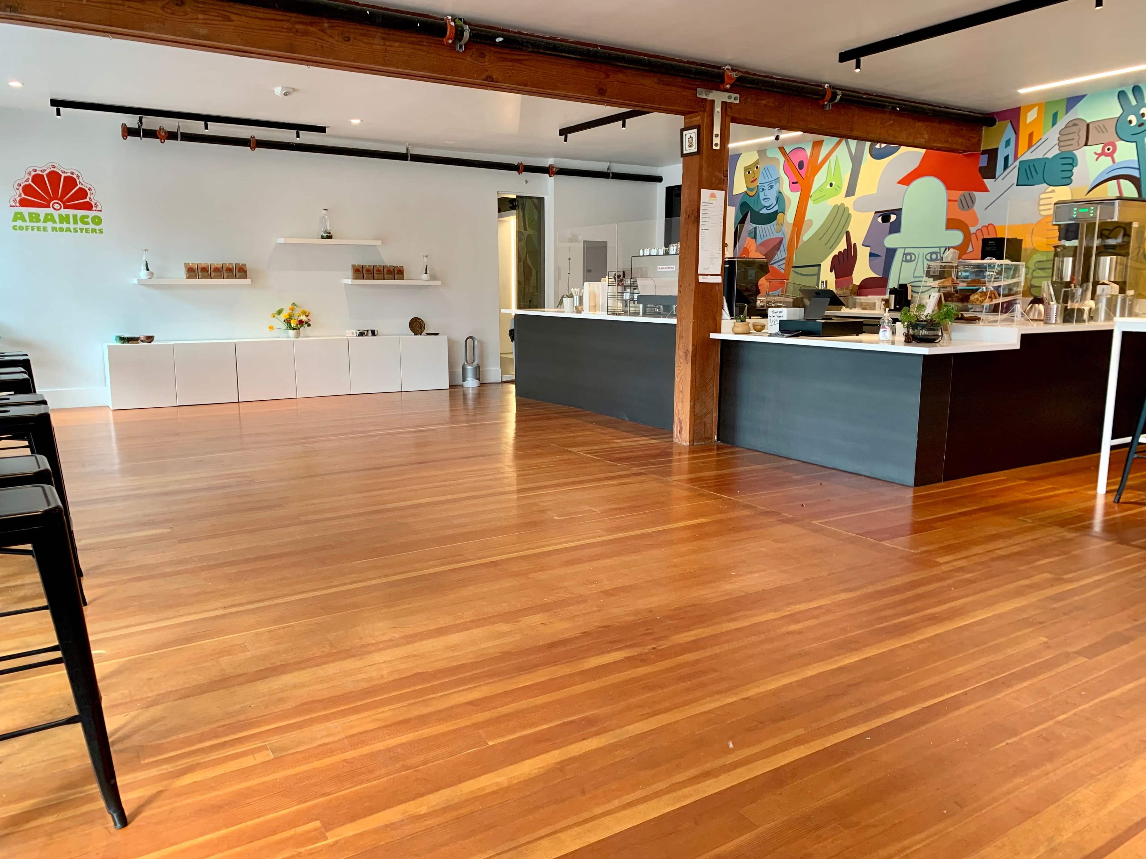 A modern coffee shop with wooden flooring, a white display area, and a colorful mural on the wall.