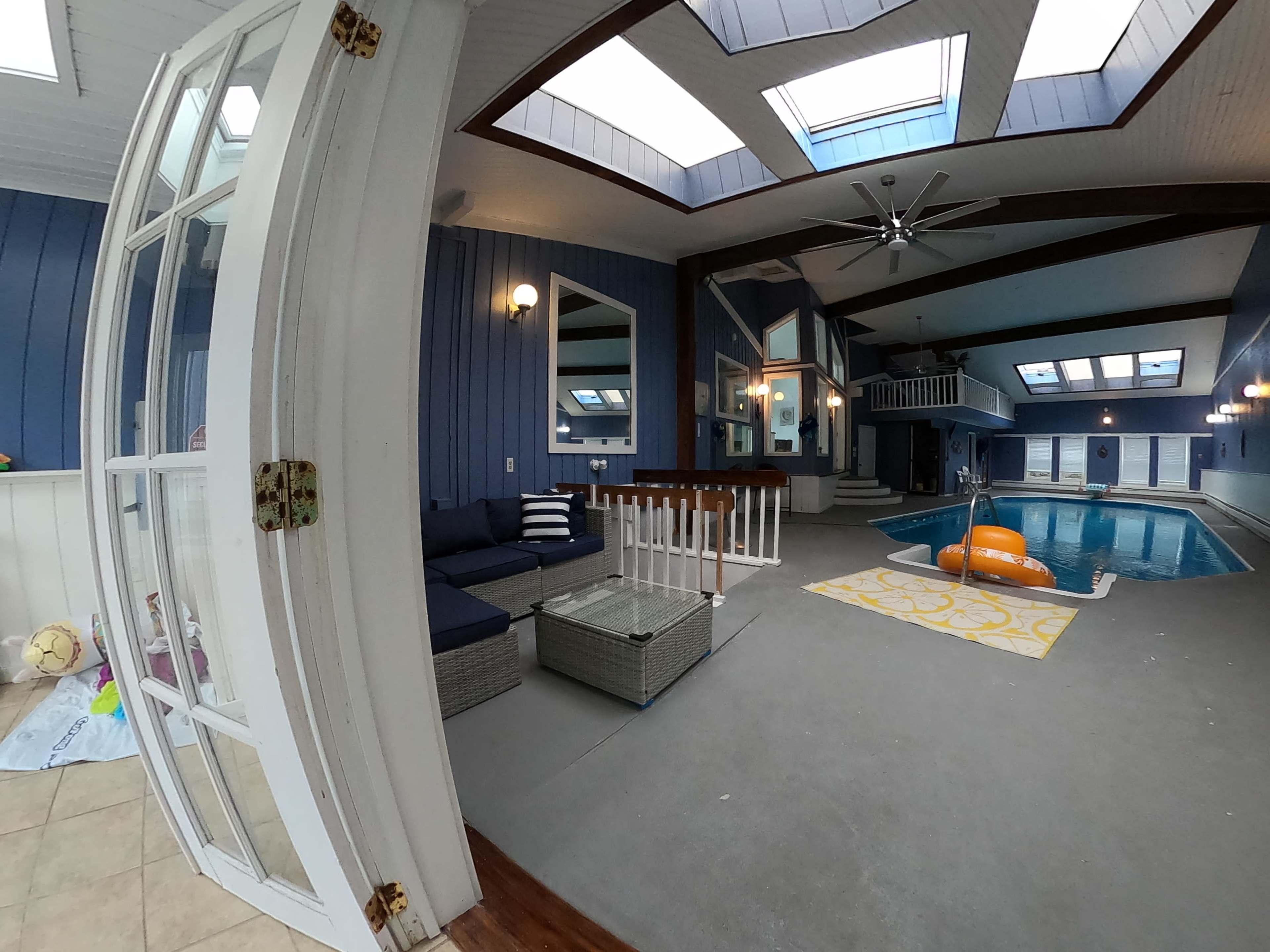 An indoor pool area with a seating arrangement, large windows, and a brightly colored inflatable in the water.