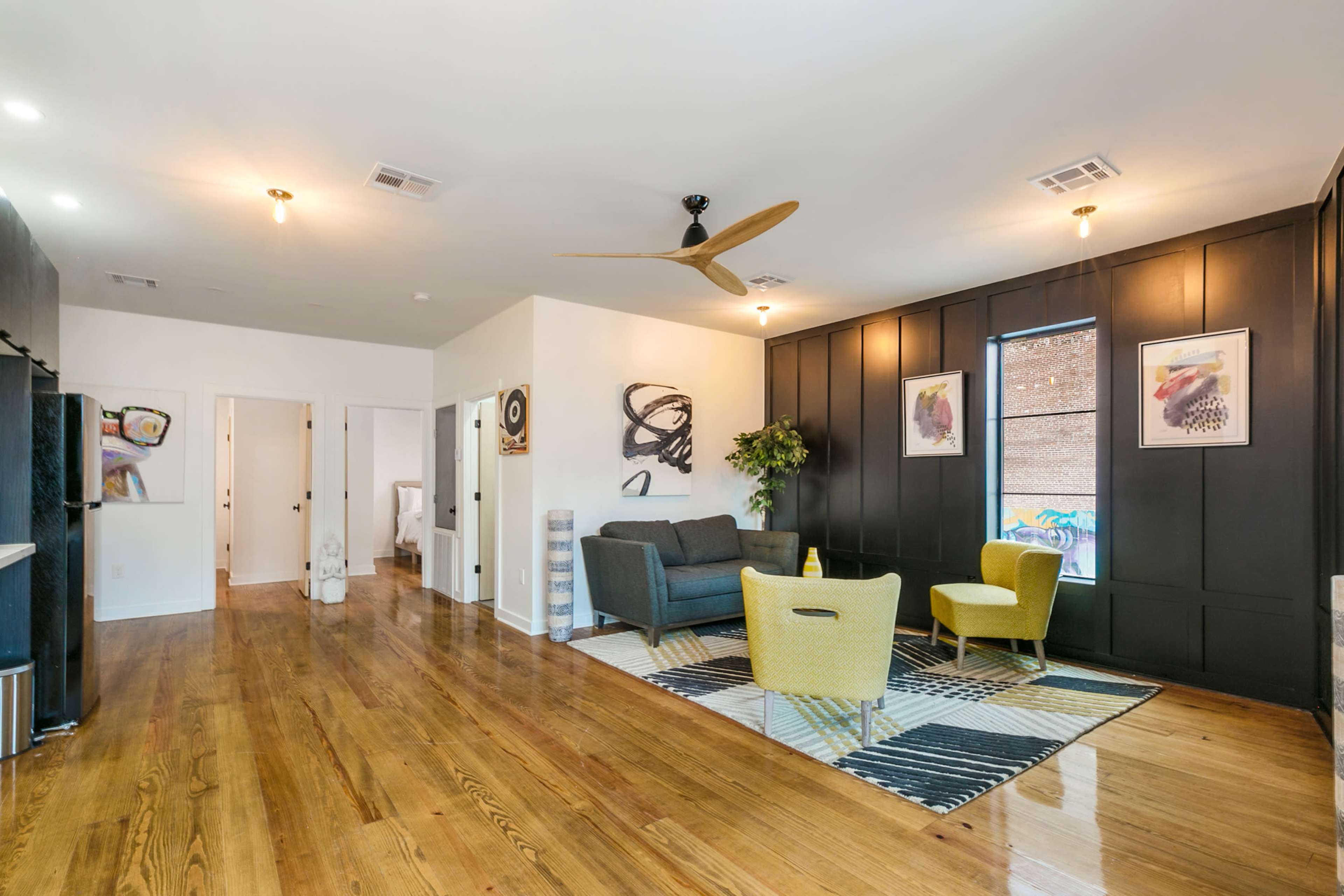 A modern living room features a gray sofa and two yellow chairs on a patterned rug, with wooden floors and a wall adorned with artwork.