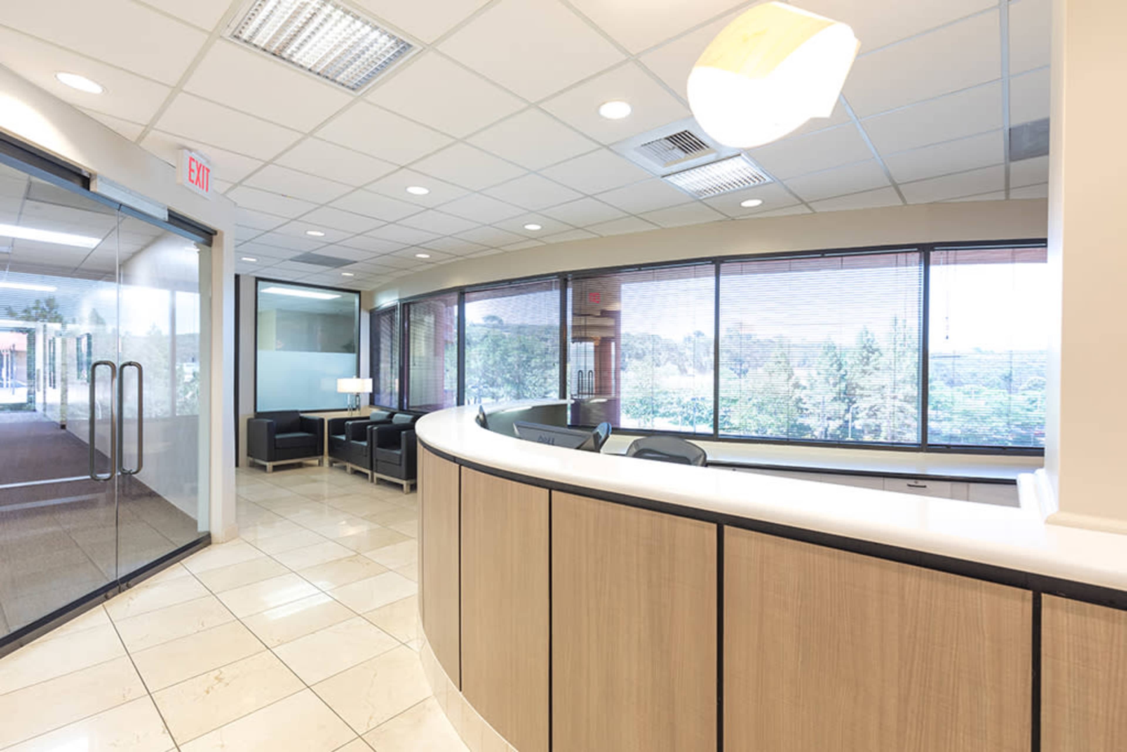 A modern reception area features a curved front desk, large windows with a view, and black seating arrangements.