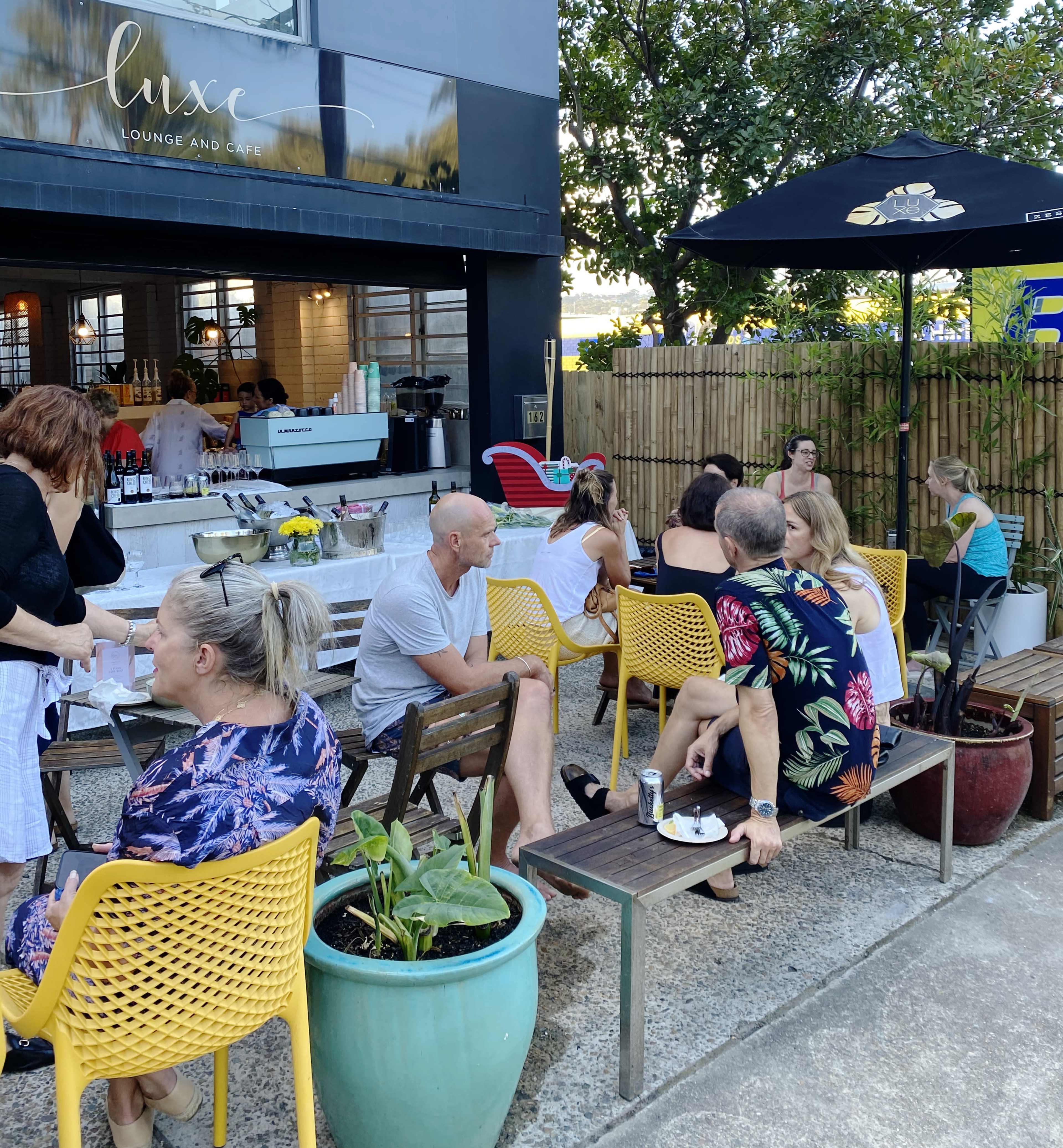 People are seated at outdoor tables in a cafe, socializing and enjoying food and drinks in a cozy courtyard setting.