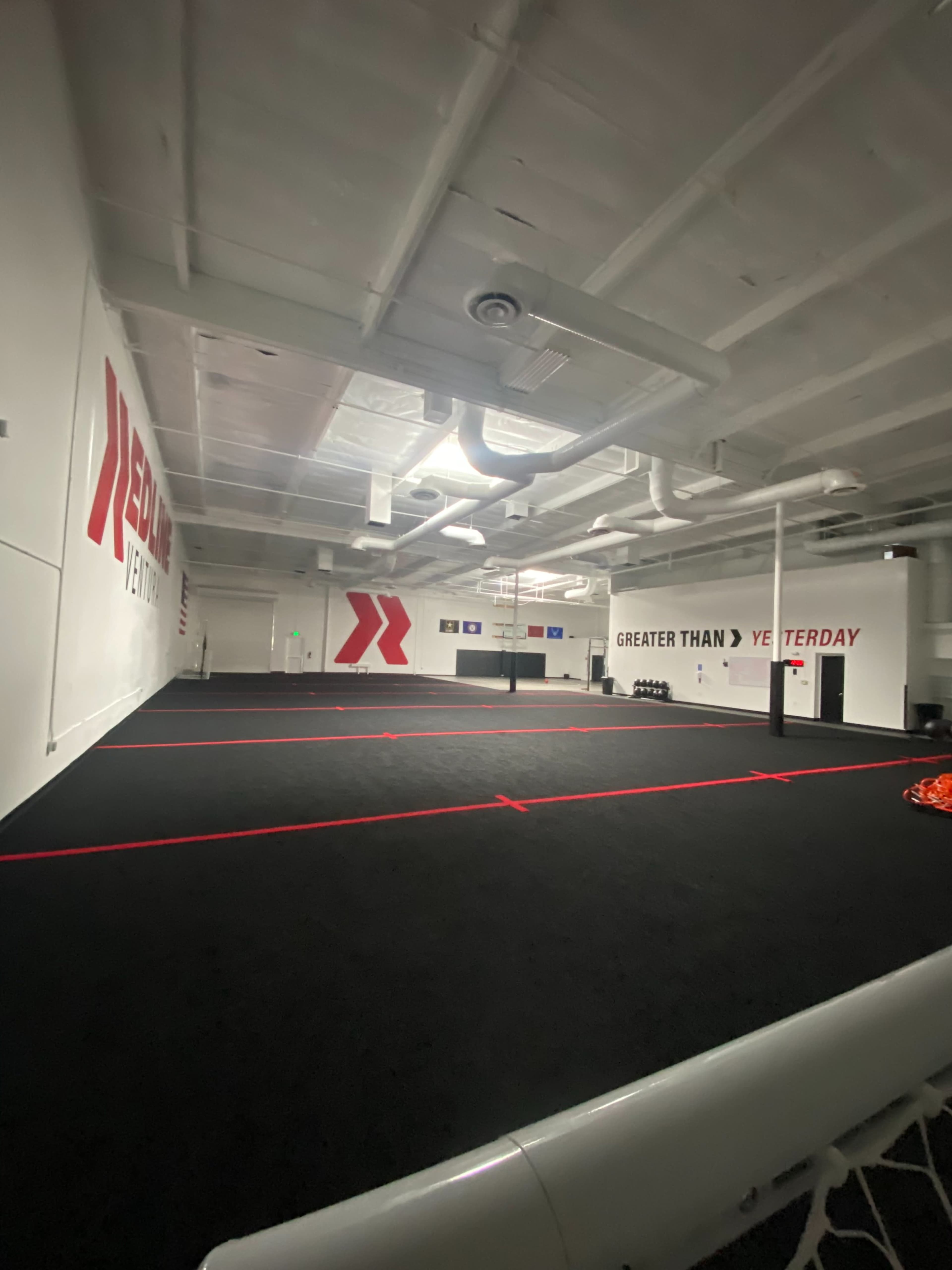 The image shows a spacious training facility with black flooring and red markings, featuring motivational wall graphics.