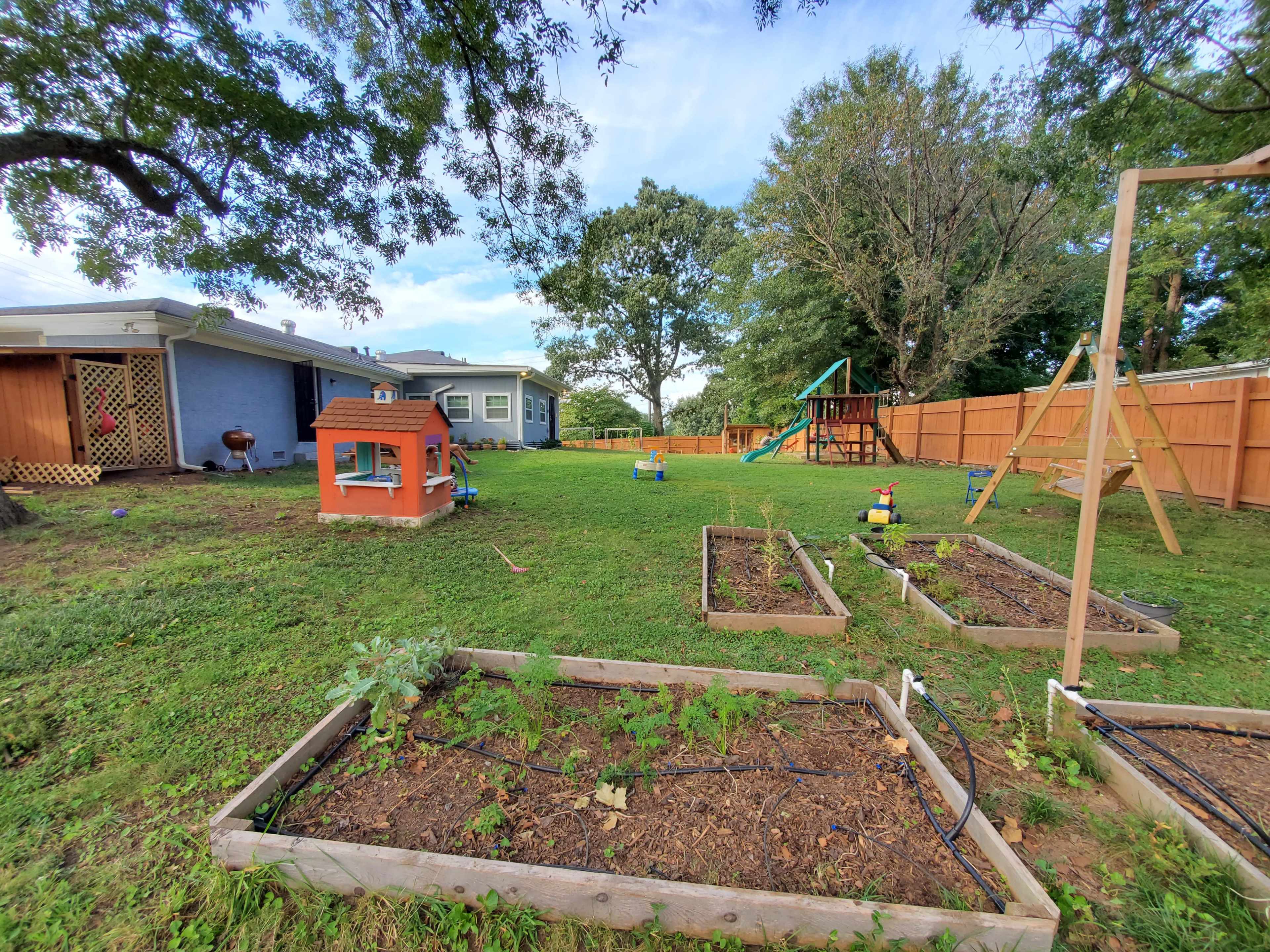 A backyard with a playset, a small playhouse, and several vegetable garden beds.