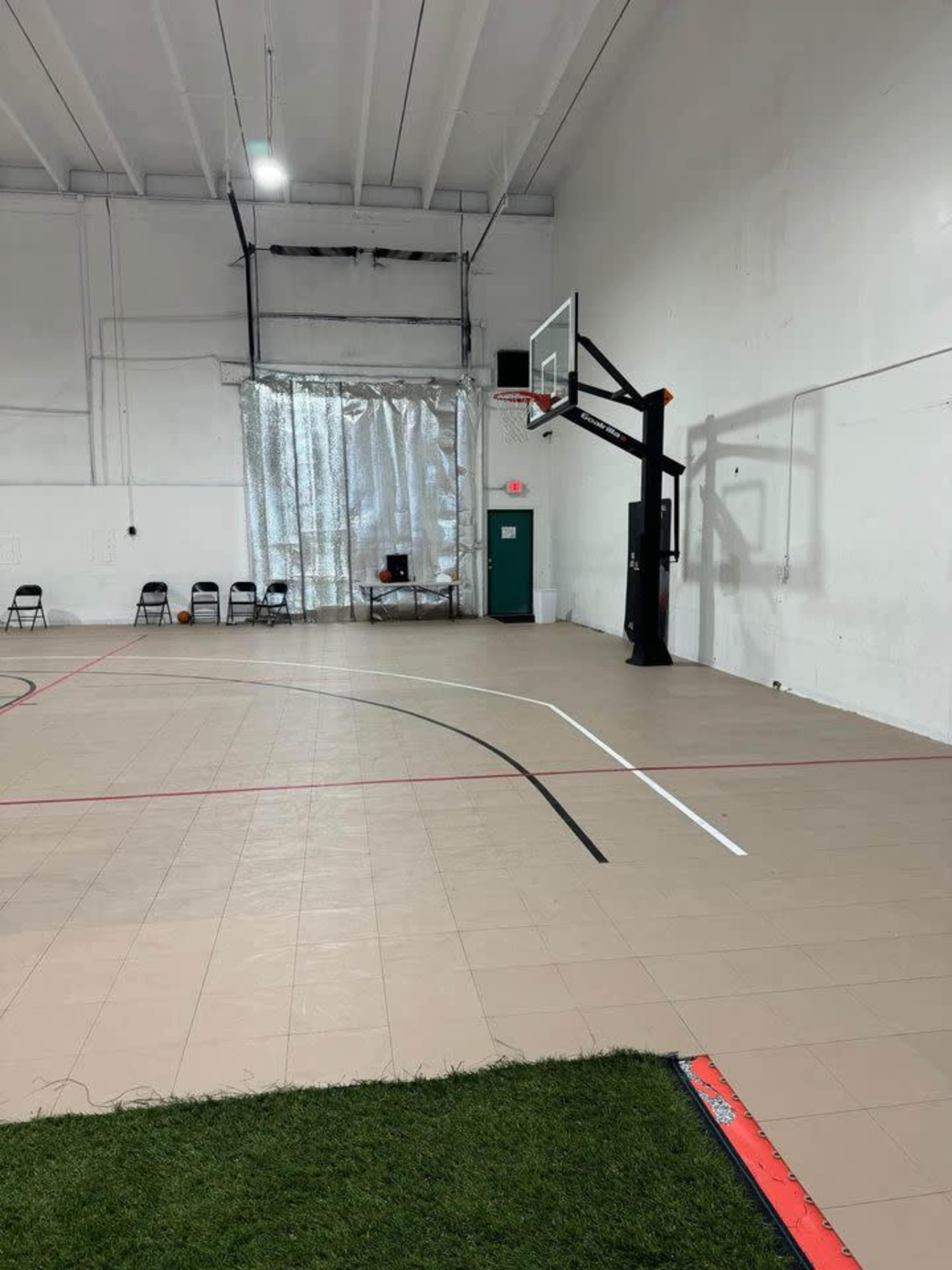 The image shows an indoor basketball court with a hoop at one end, surrounded by a smooth floor and chairs positioned along the sidelines.