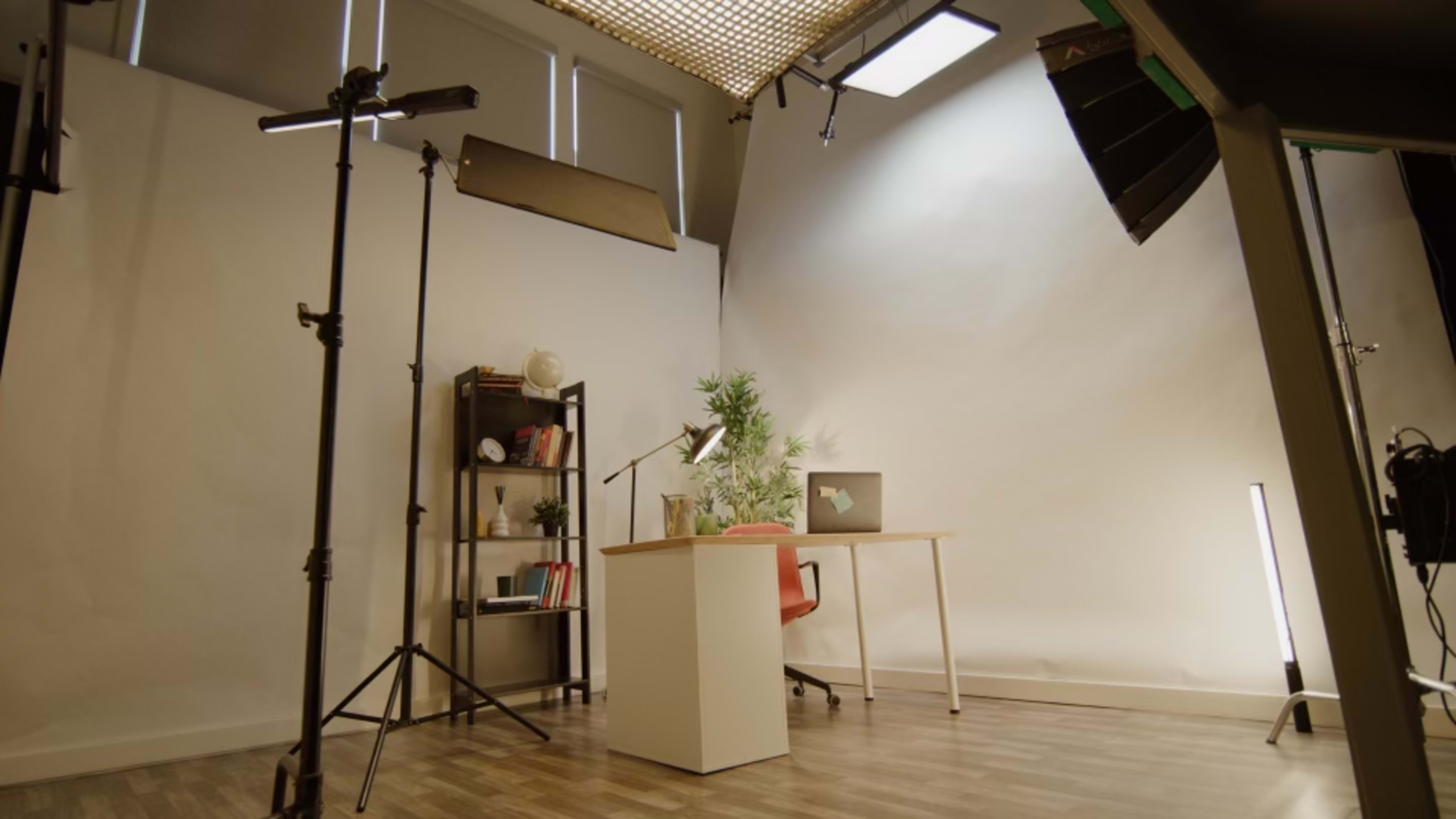 A photography studio setup with a desk, chair, lighting equipment, and a backdrop.
