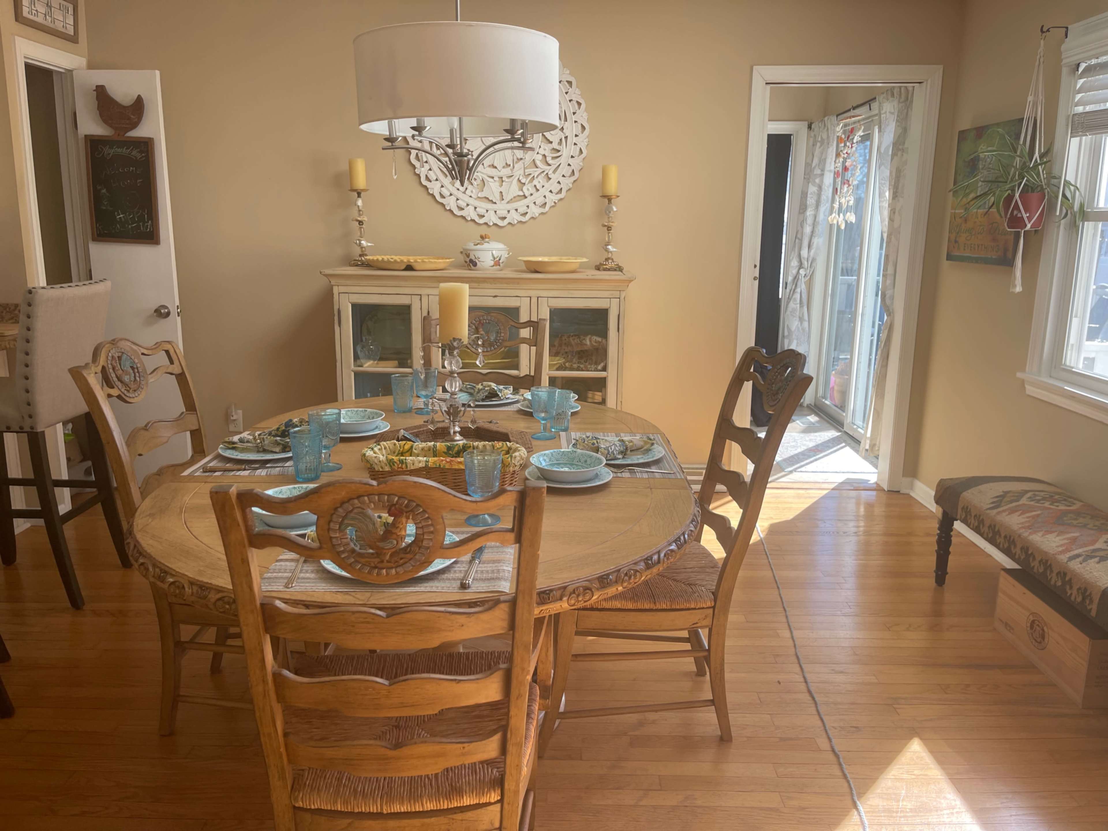 A round dining table is set with plates and glasses in a bright room featuring a cabinet and sliding glass doors.