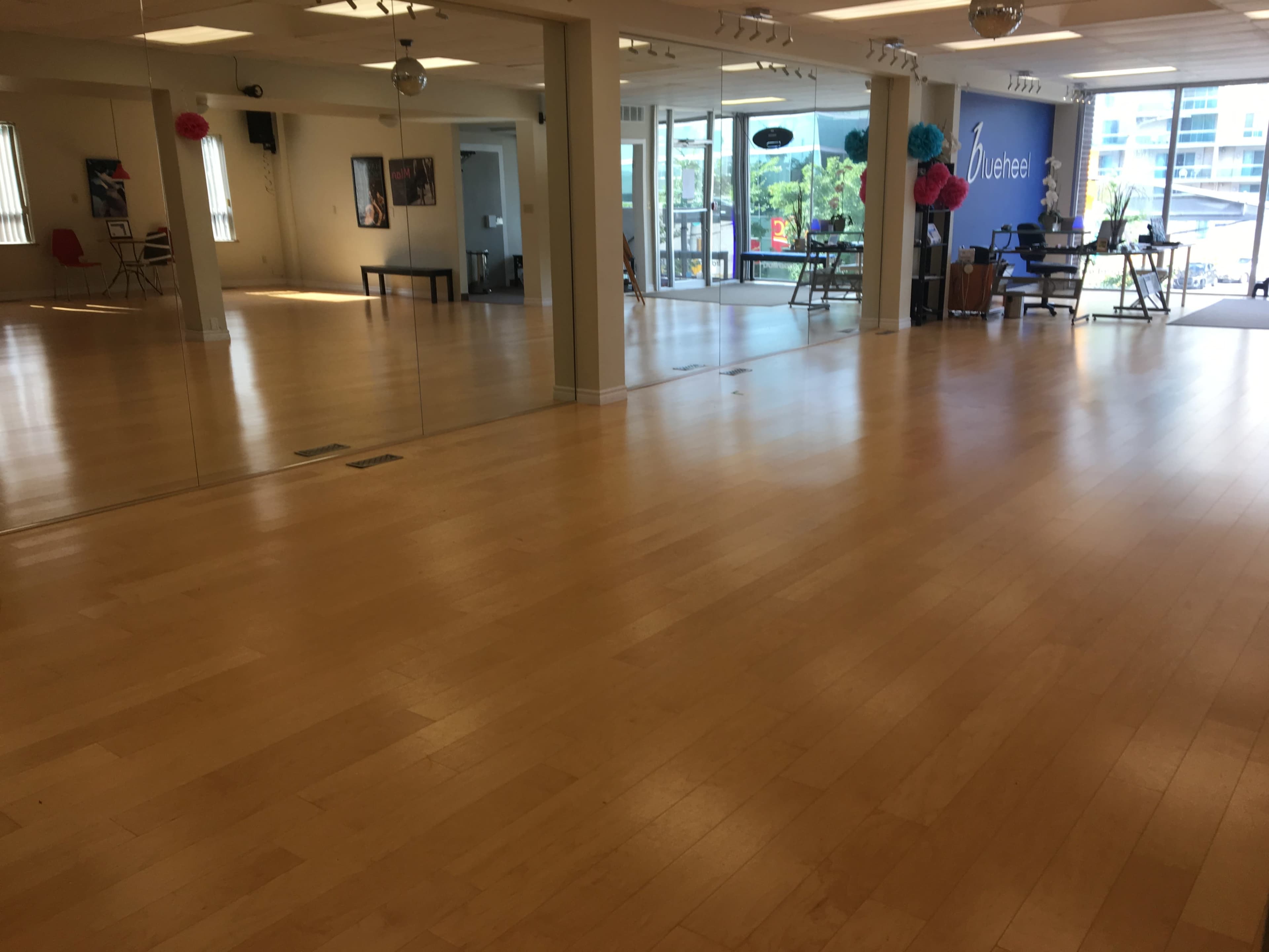 A spacious studio with wooden flooring, large windows, and a mirrored wall.
