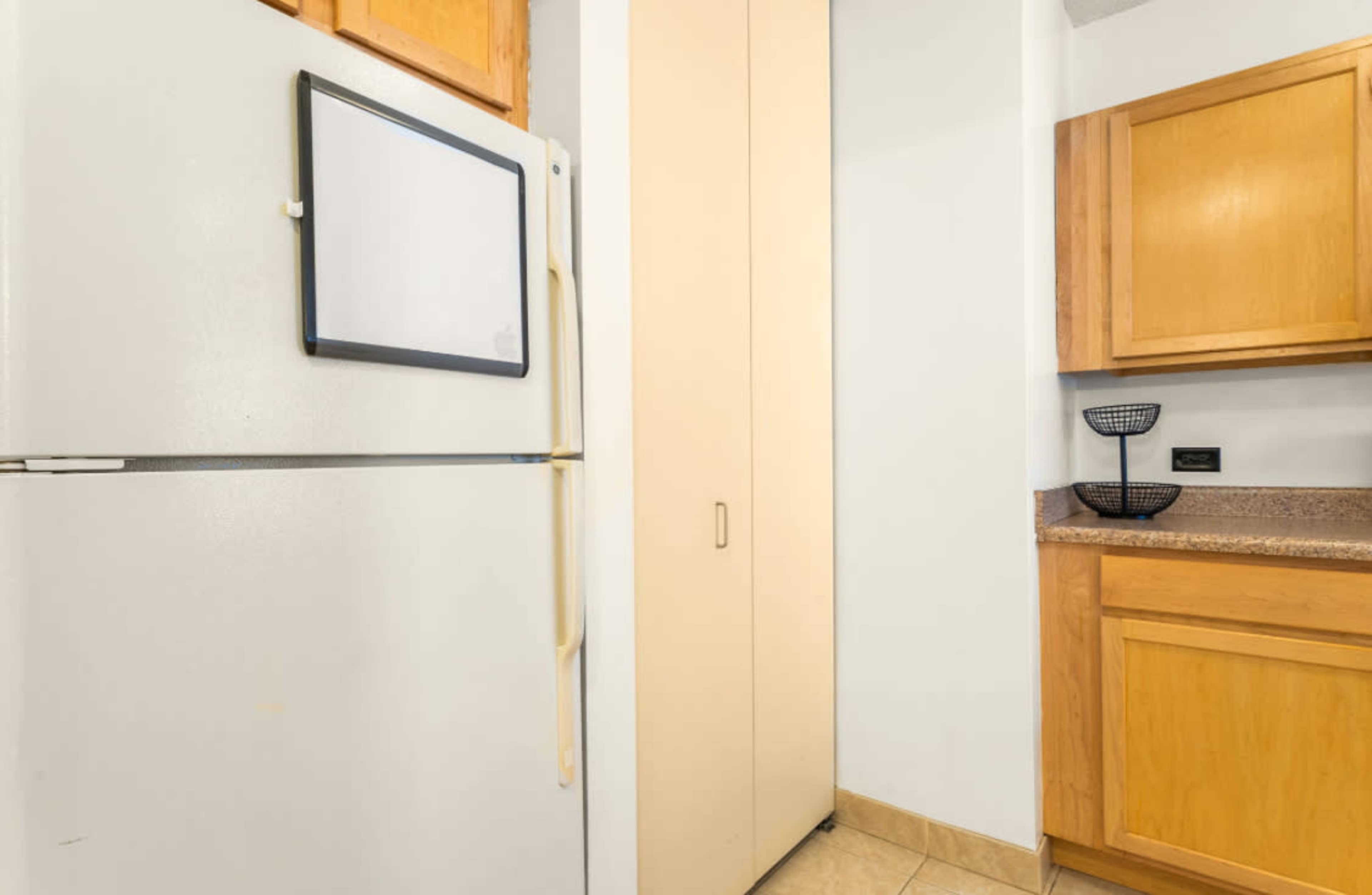 The image shows a white refrigerator next to a tall, beige storage cabinet in a kitchen with wooden cabinets and a countertop.