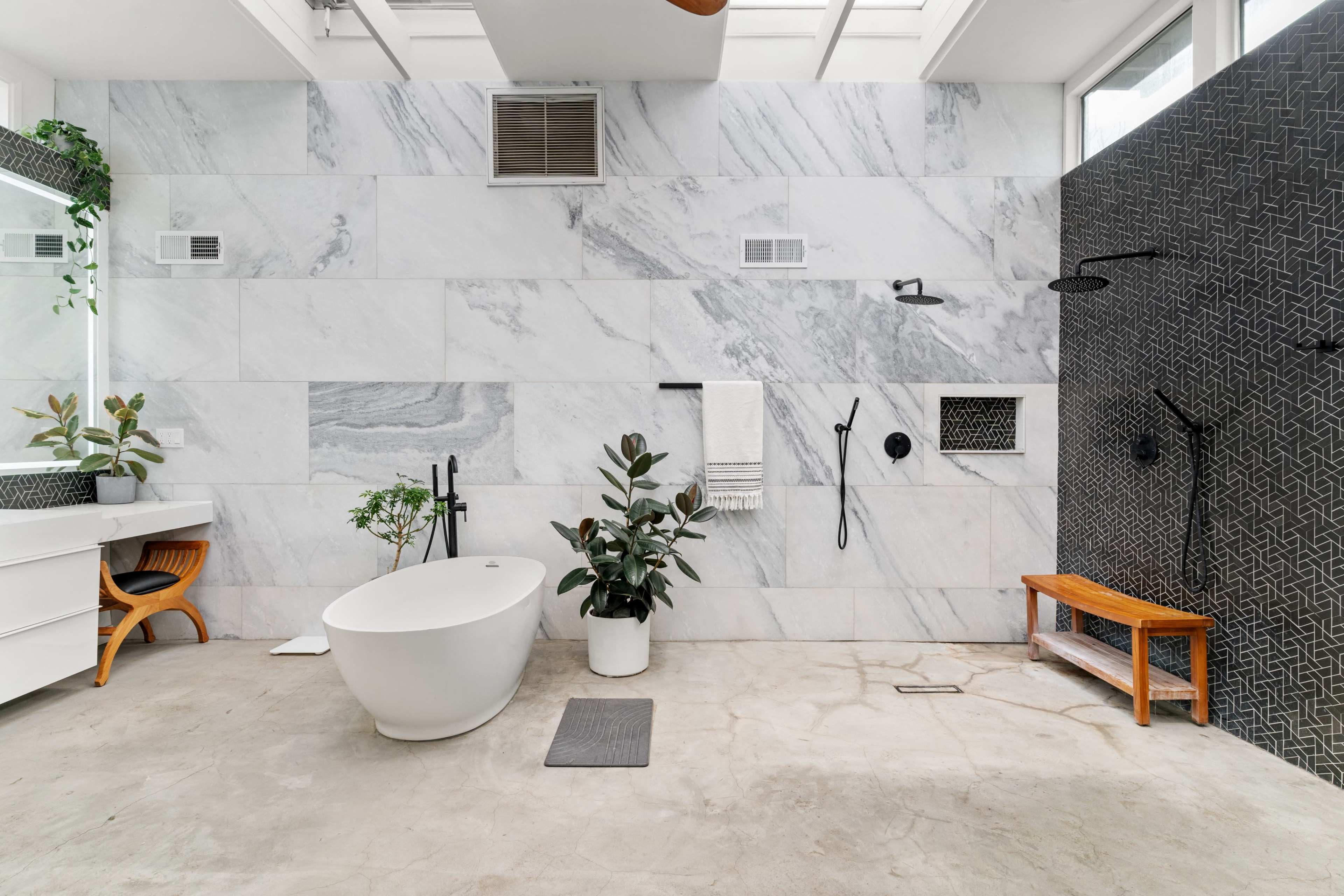 A modern bathroom featuring a freestanding bathtub, a dark accent wall with shower fixtures, and a large marble wall with plant decorations.