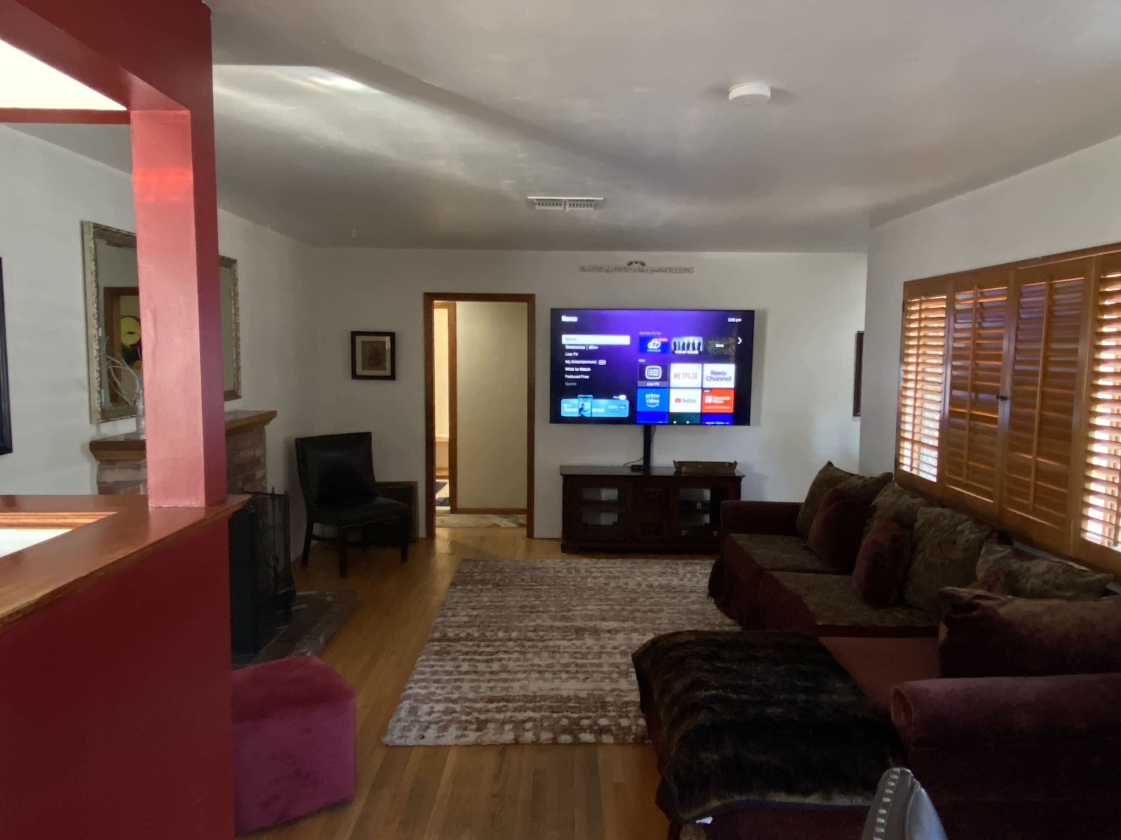 The image shows a living room with a dark-colored sofa, a television on a stand, and wooden shutters on the windows.