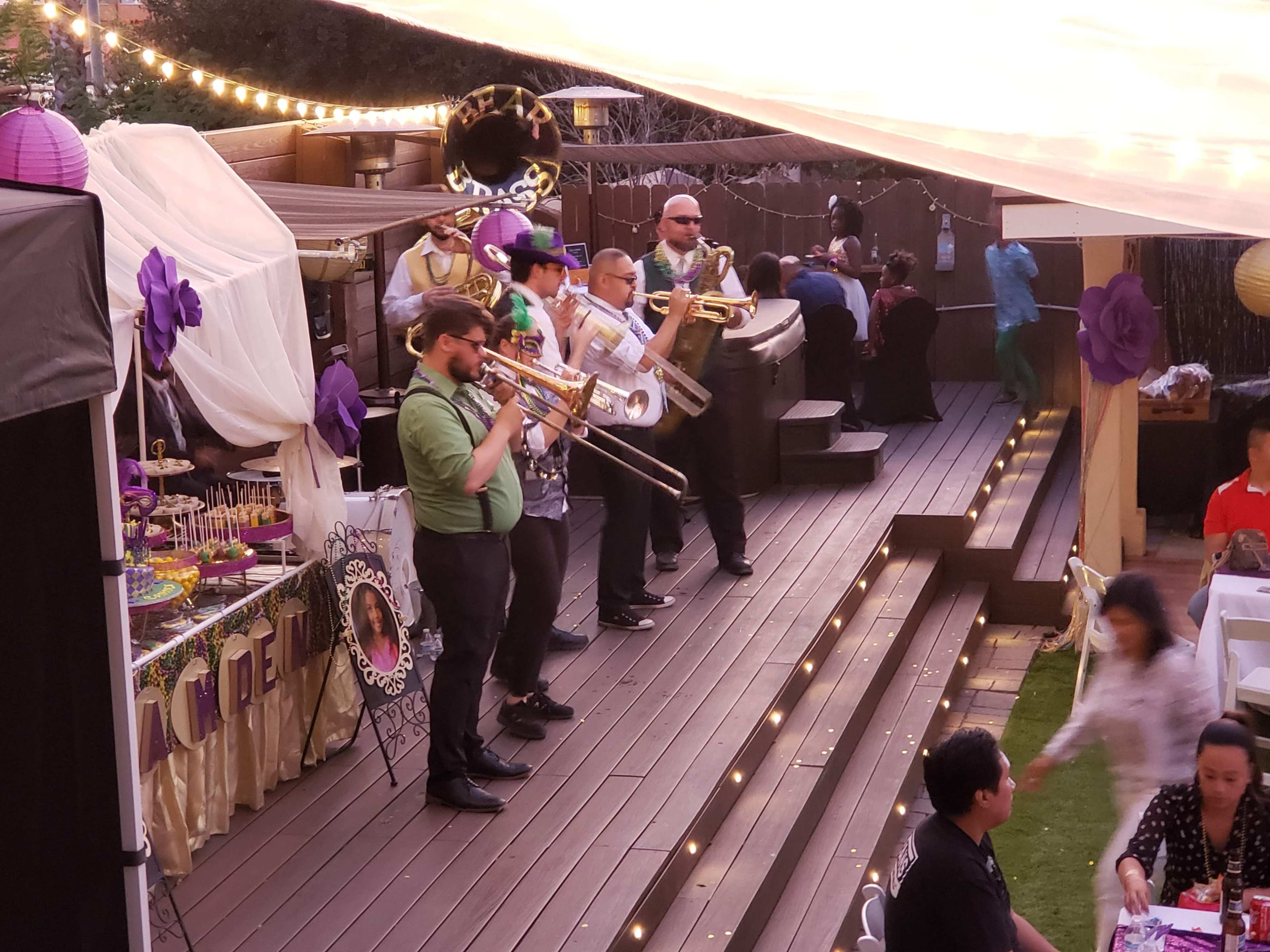 A brass band performs on a wooden deck at a festive gathering adorned with decorations and tables.