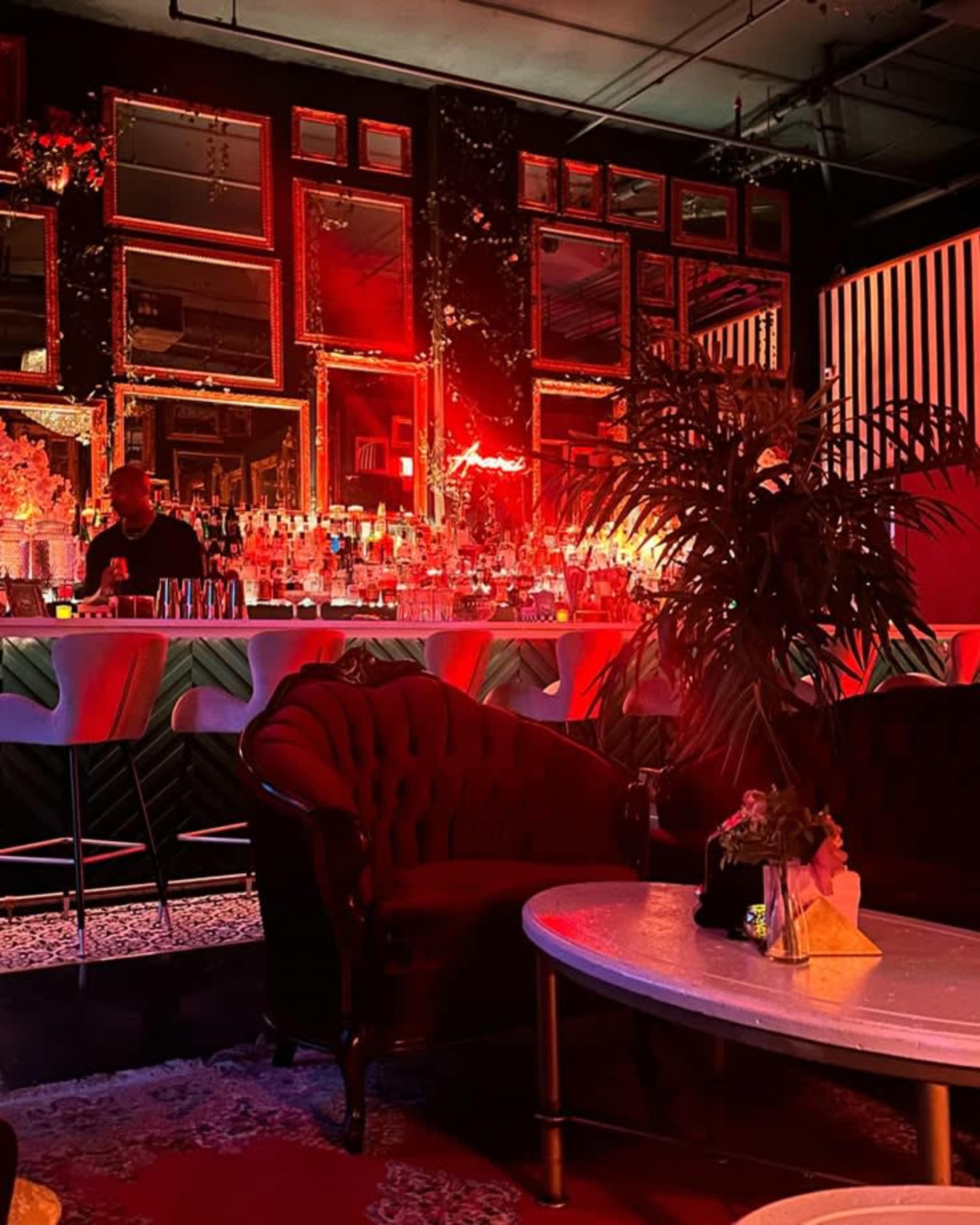 The image shows a dimly lit bar with ornate mirrors on the walls, a well-stocked bar counter, and plush seating.
