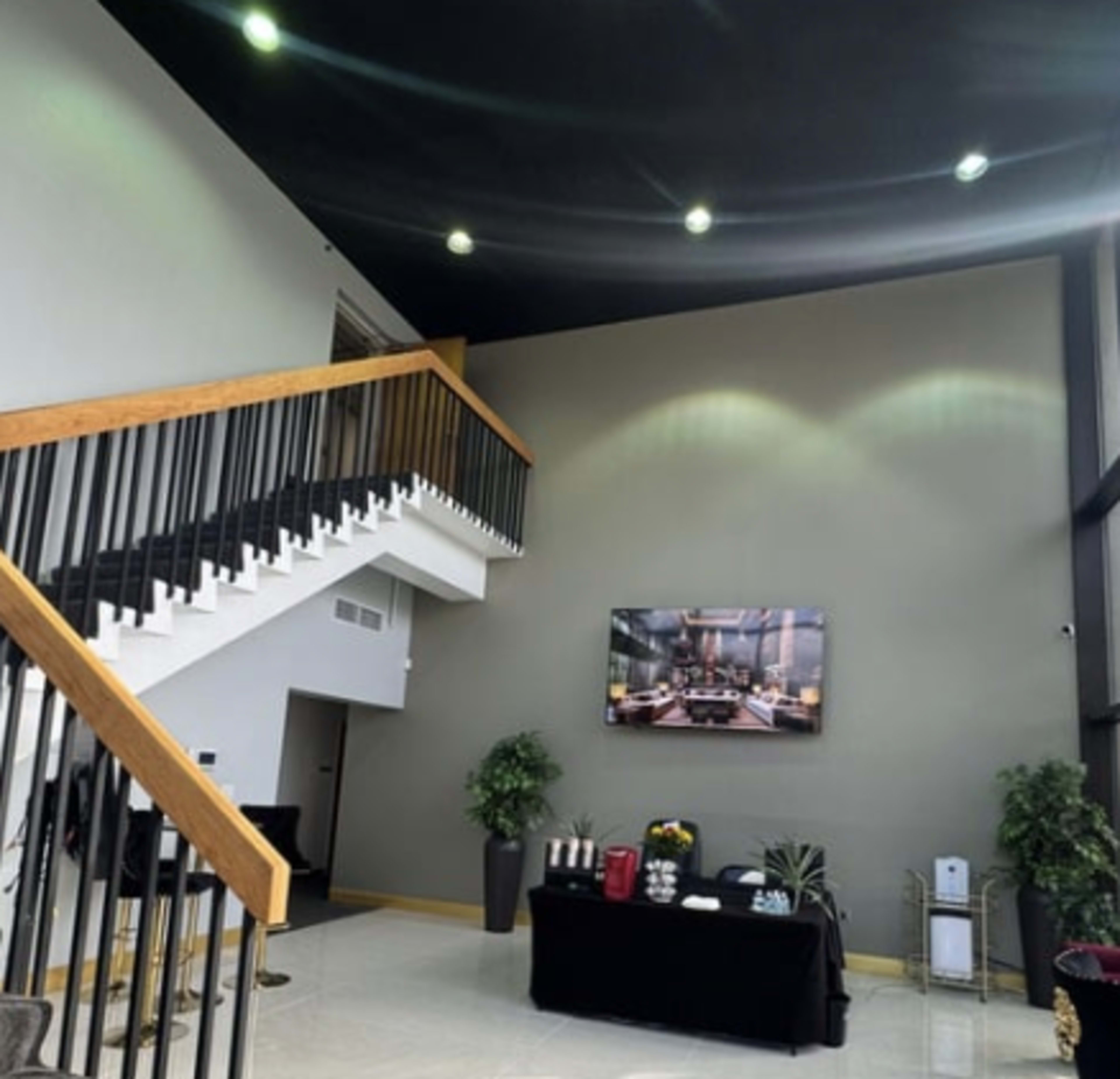 The image shows a modern lobby with a staircase and a large wall-mounted television displaying a dining setting.