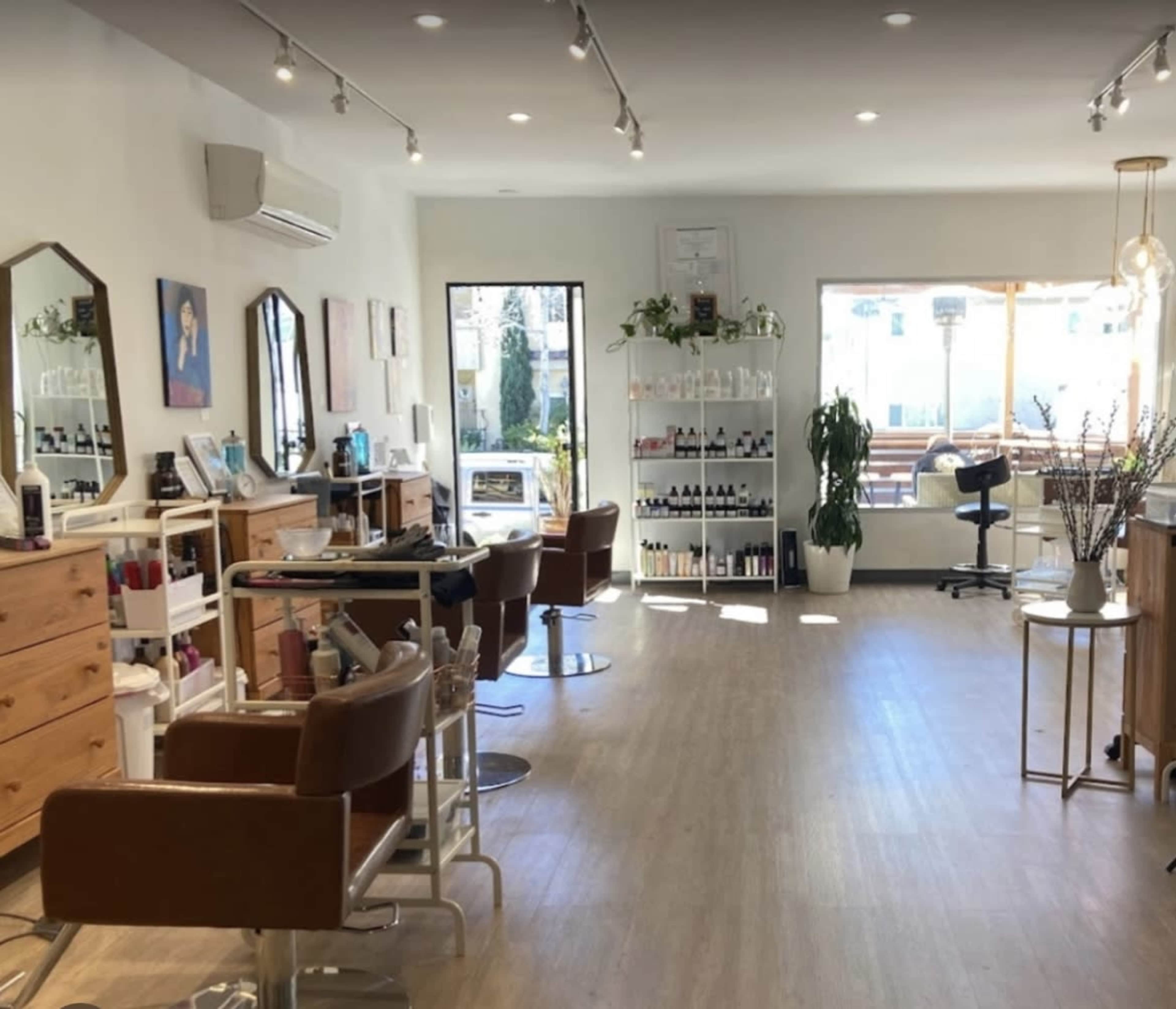 A bright salon interior with multiple styling stations, mirrors, and shelves displaying hair products.