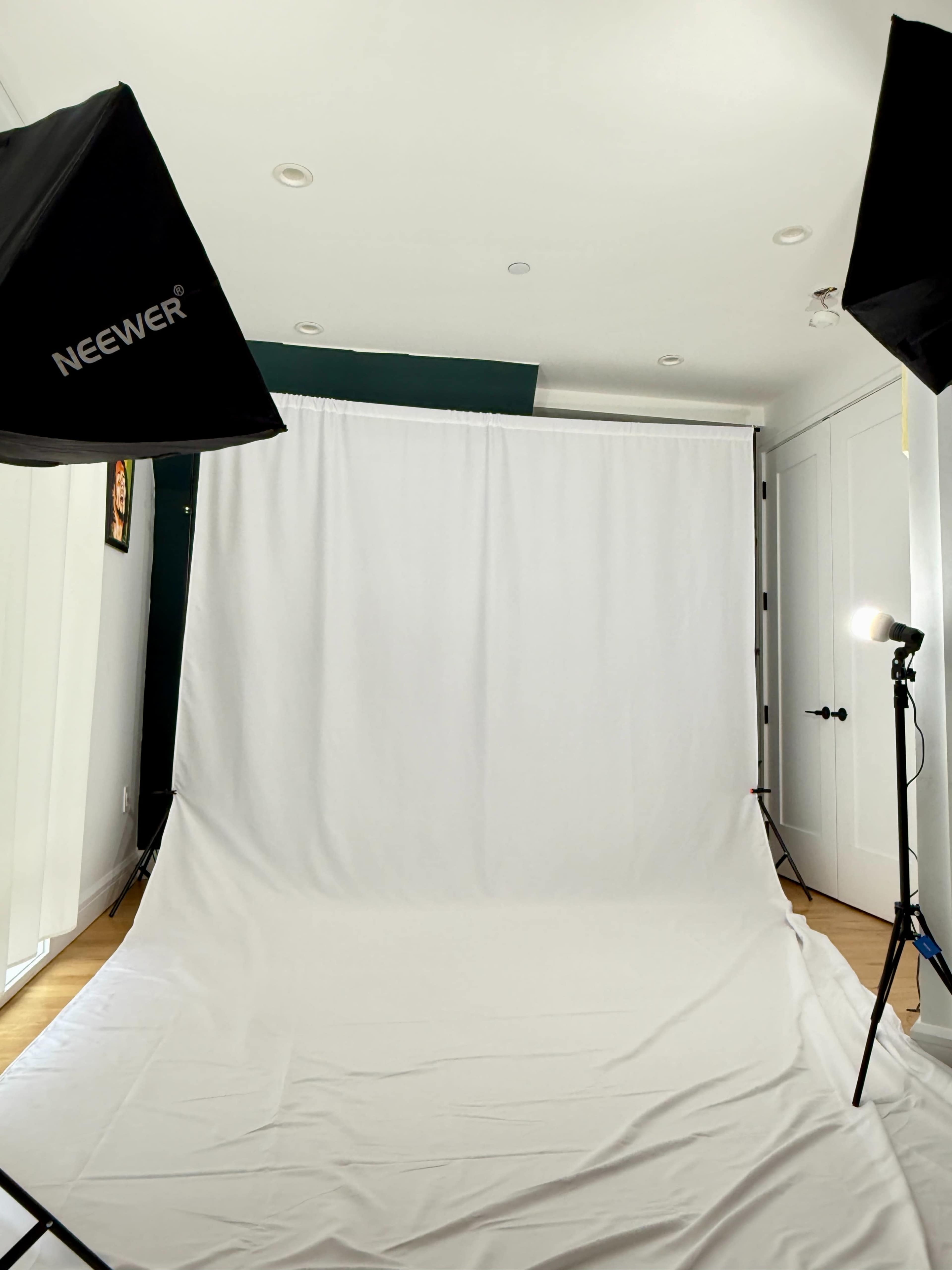 The image shows a photography studio setup with a plain white backdrop and two lighting stands positioned on either side.