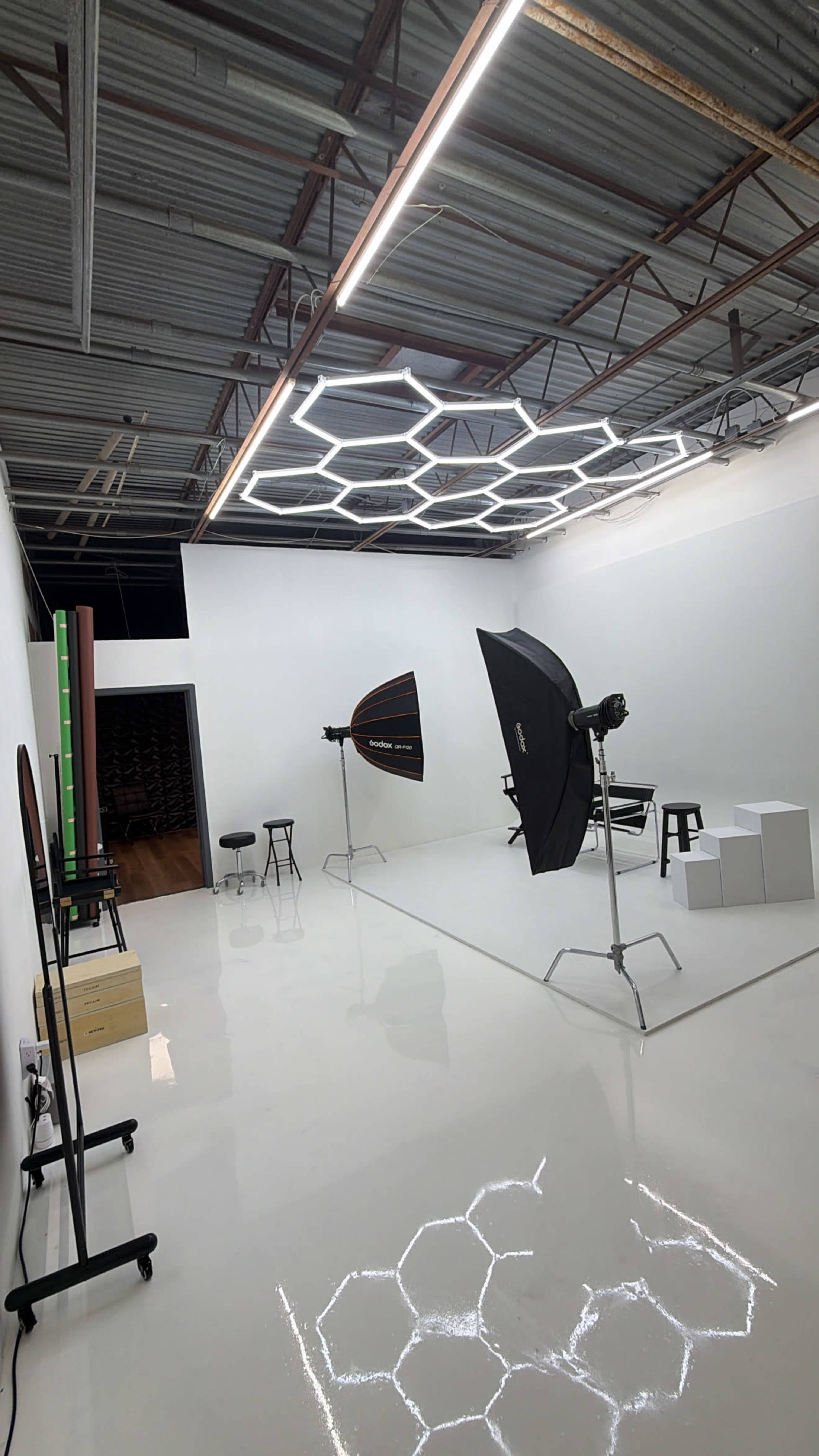 The image shows a photo studio with various lighting equipment, a few stools, and a backdrop, all set up in a spacious, minimalist environment.