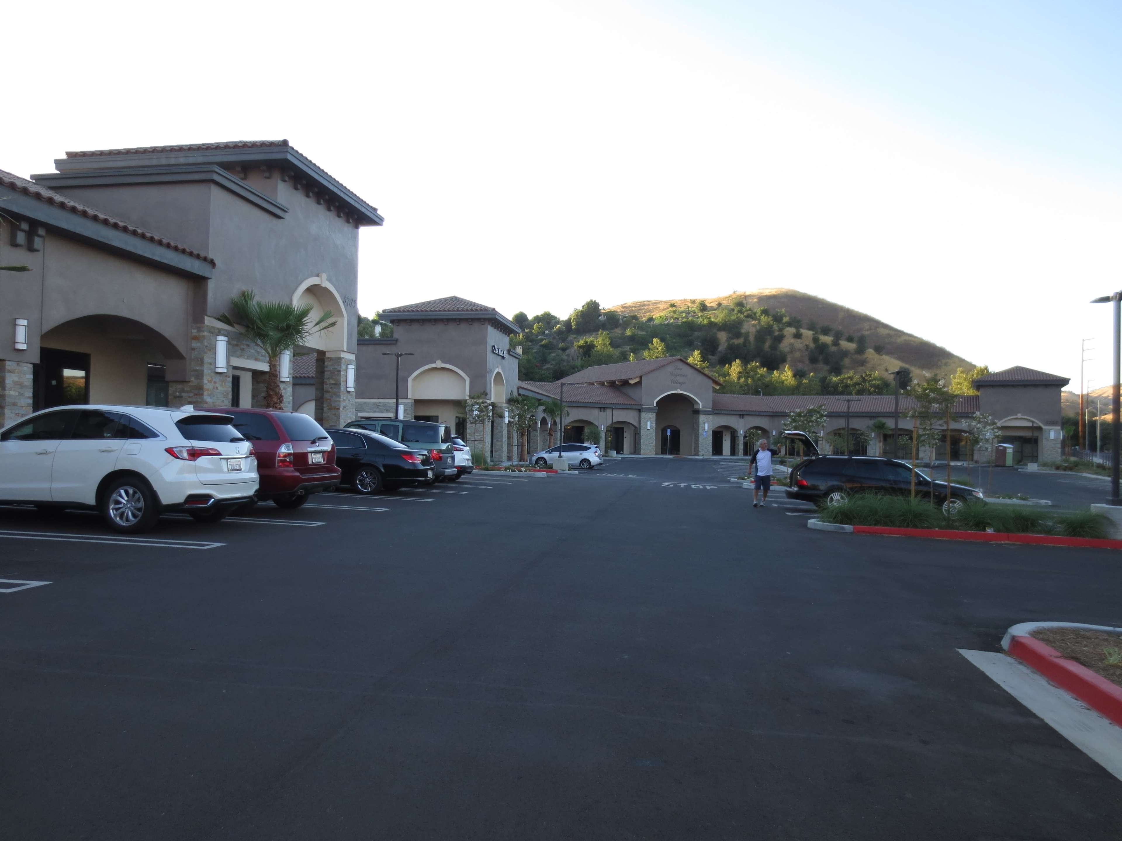 The image shows a parking lot in front of a set of buildings with a hillside in the background.