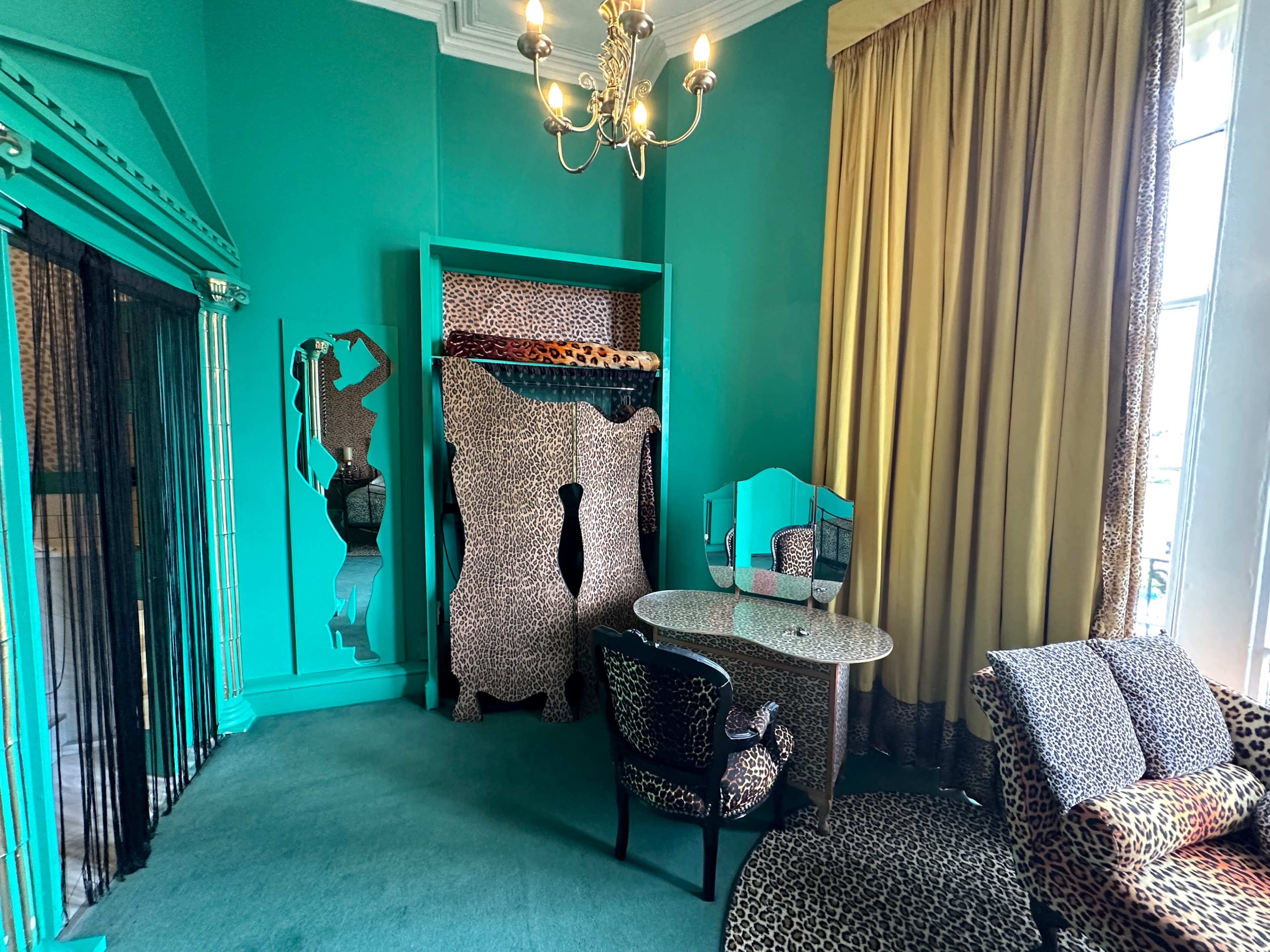 A room with turquoise walls and leopard print furnishings, including a table and a chair, along with a bed in the corner.