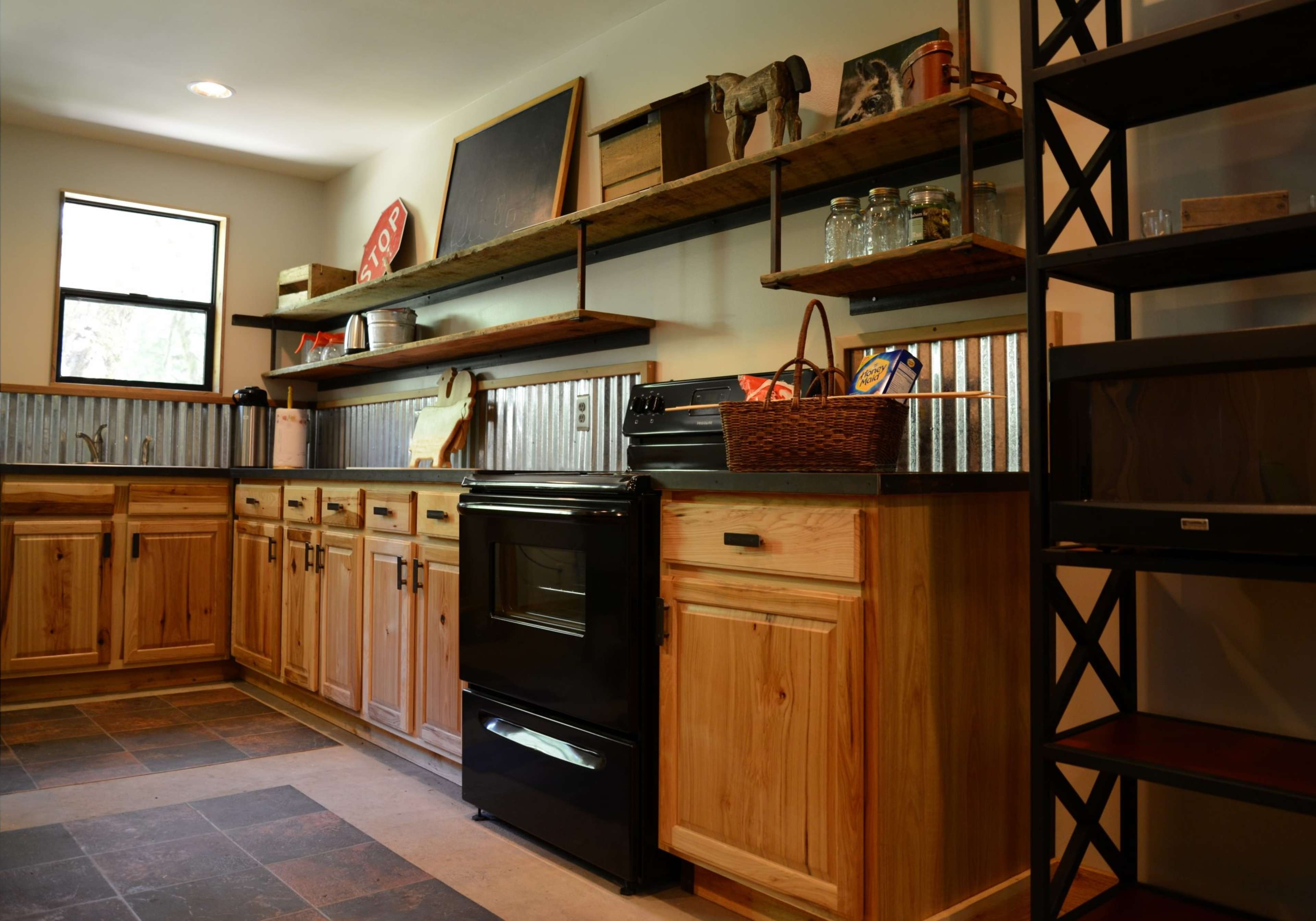 A kitchen with wooden cabinets, metal shelving, a black stove, and a window providing natural light.