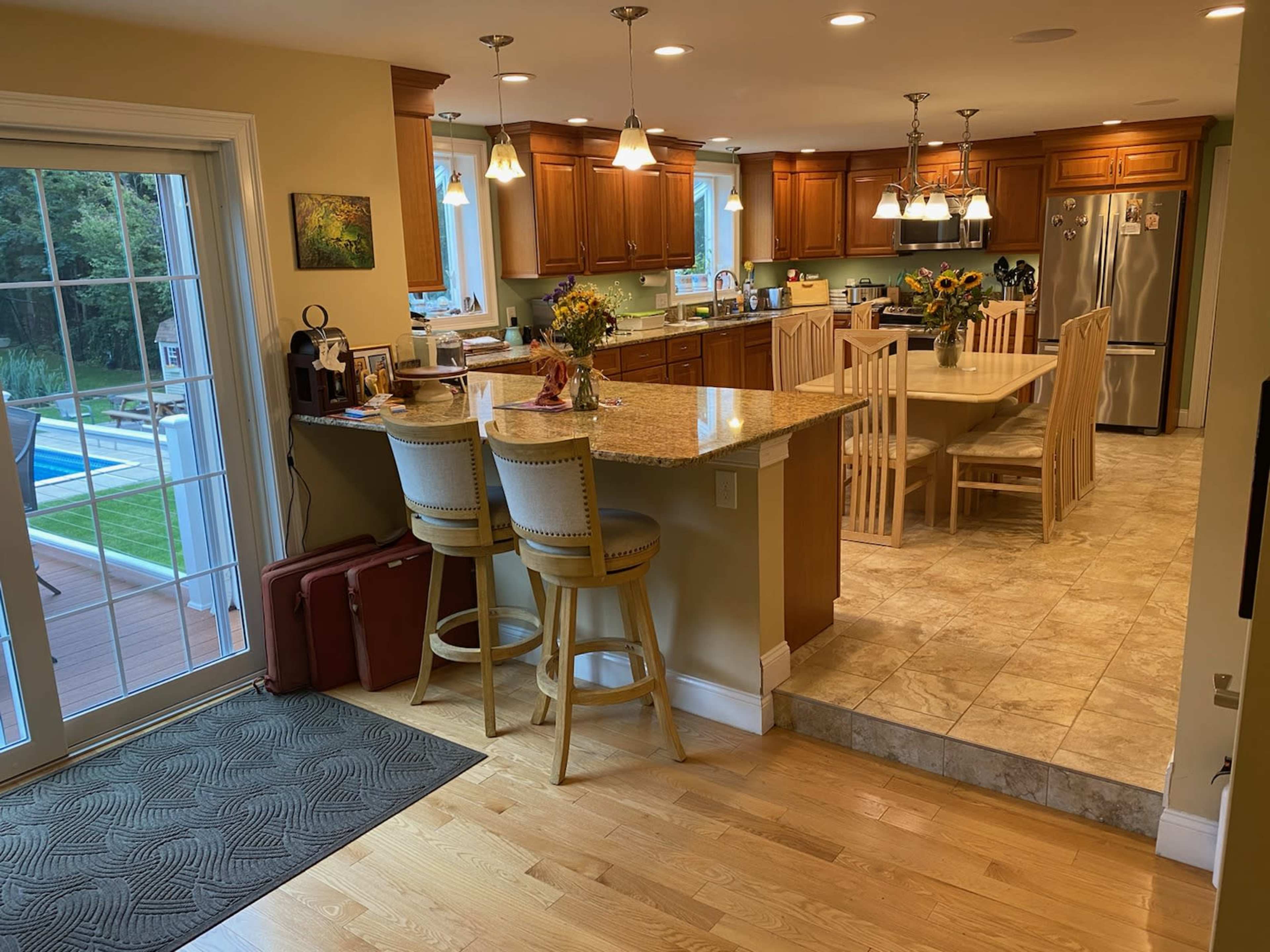 A kitchen features wooden cabinetry, a central island with bar stools, and a view of an outdoor pool area through large sliding glass doors.