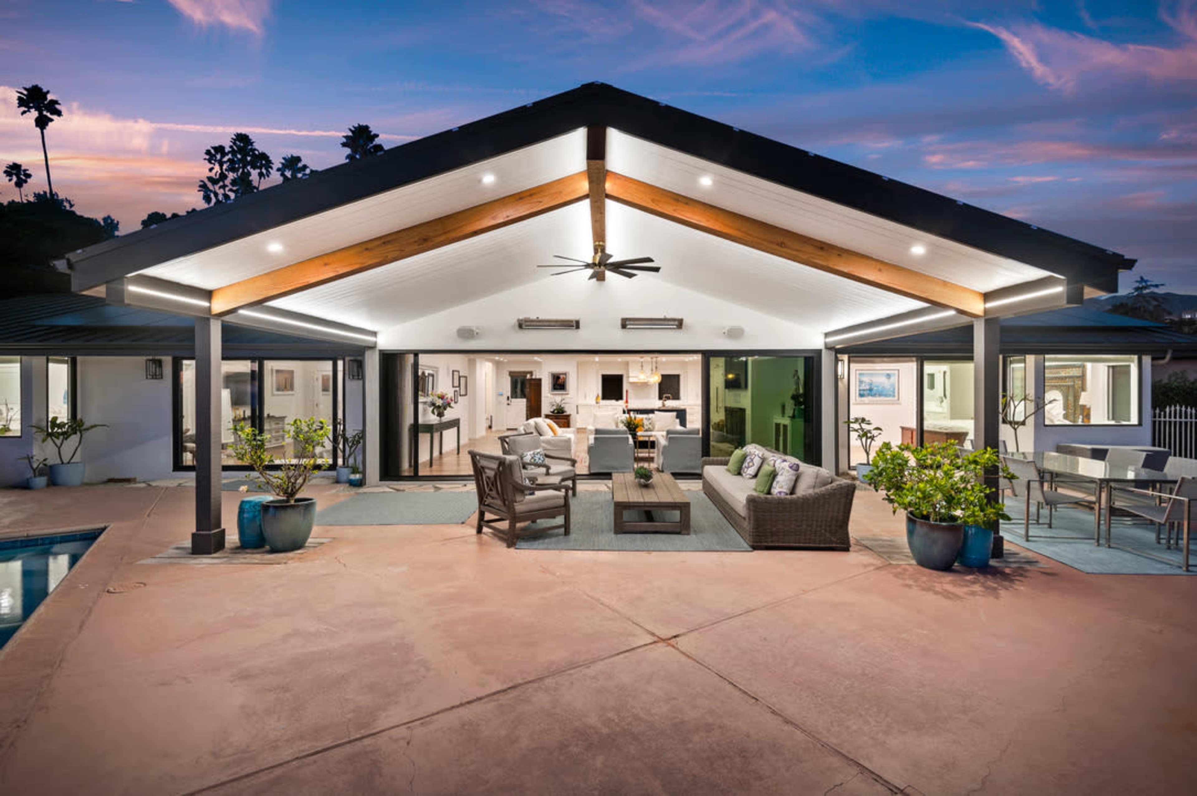 A modern, outdoor living space with a covered patio, swimming pool, and stylish furniture, set against a twilight sky.